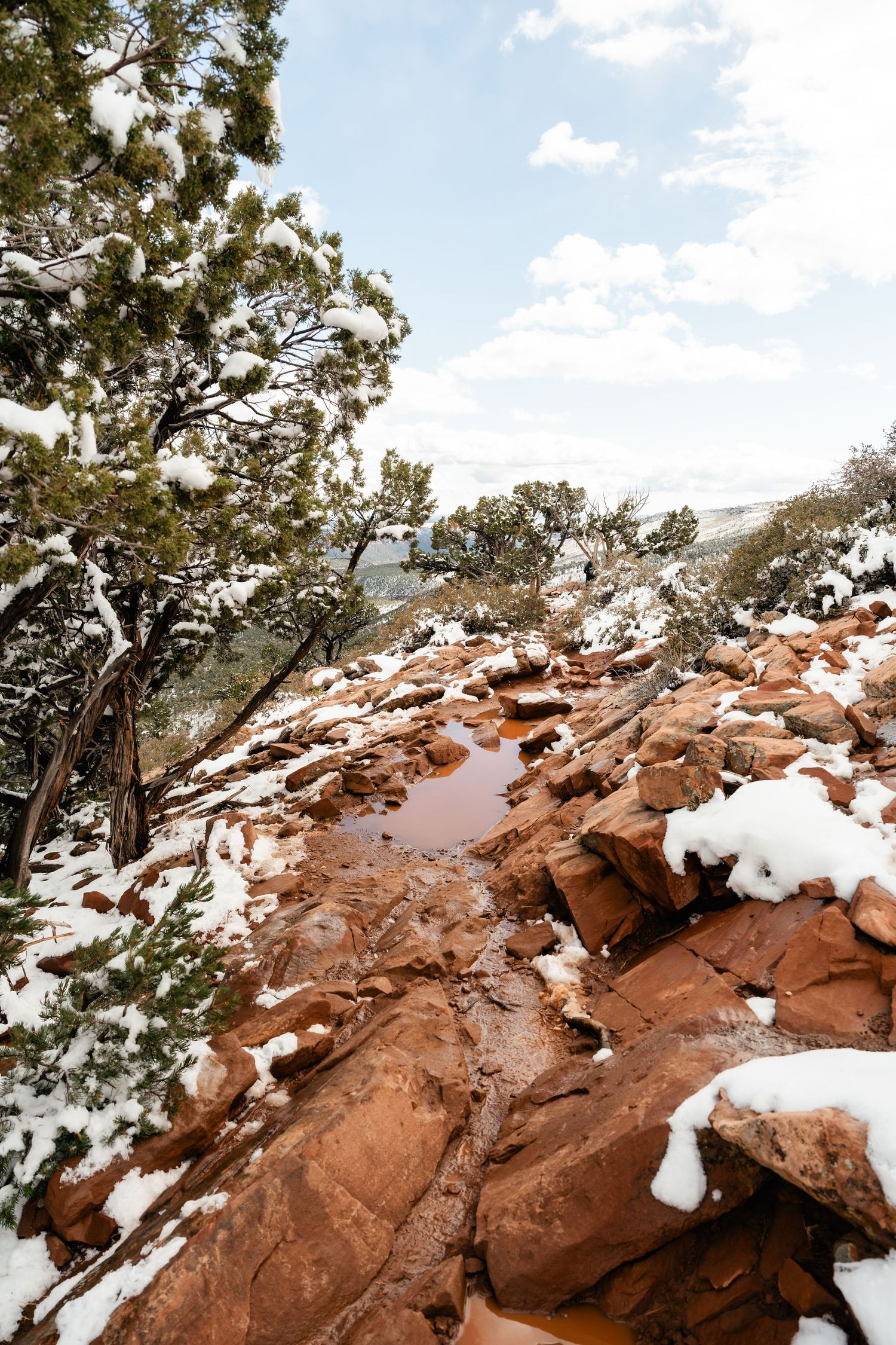 Snow dusted red rock formations and juniper trees create a dramatic winter landscape in the desert.