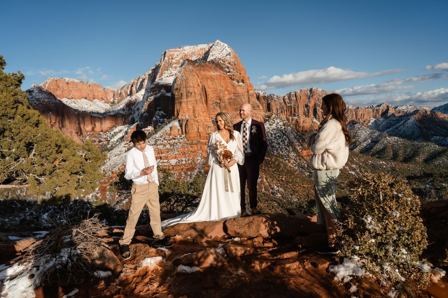 A winter wedding photoshoot against dramatic red rock cliffs and snowy terrain in Sedona, Arizona.