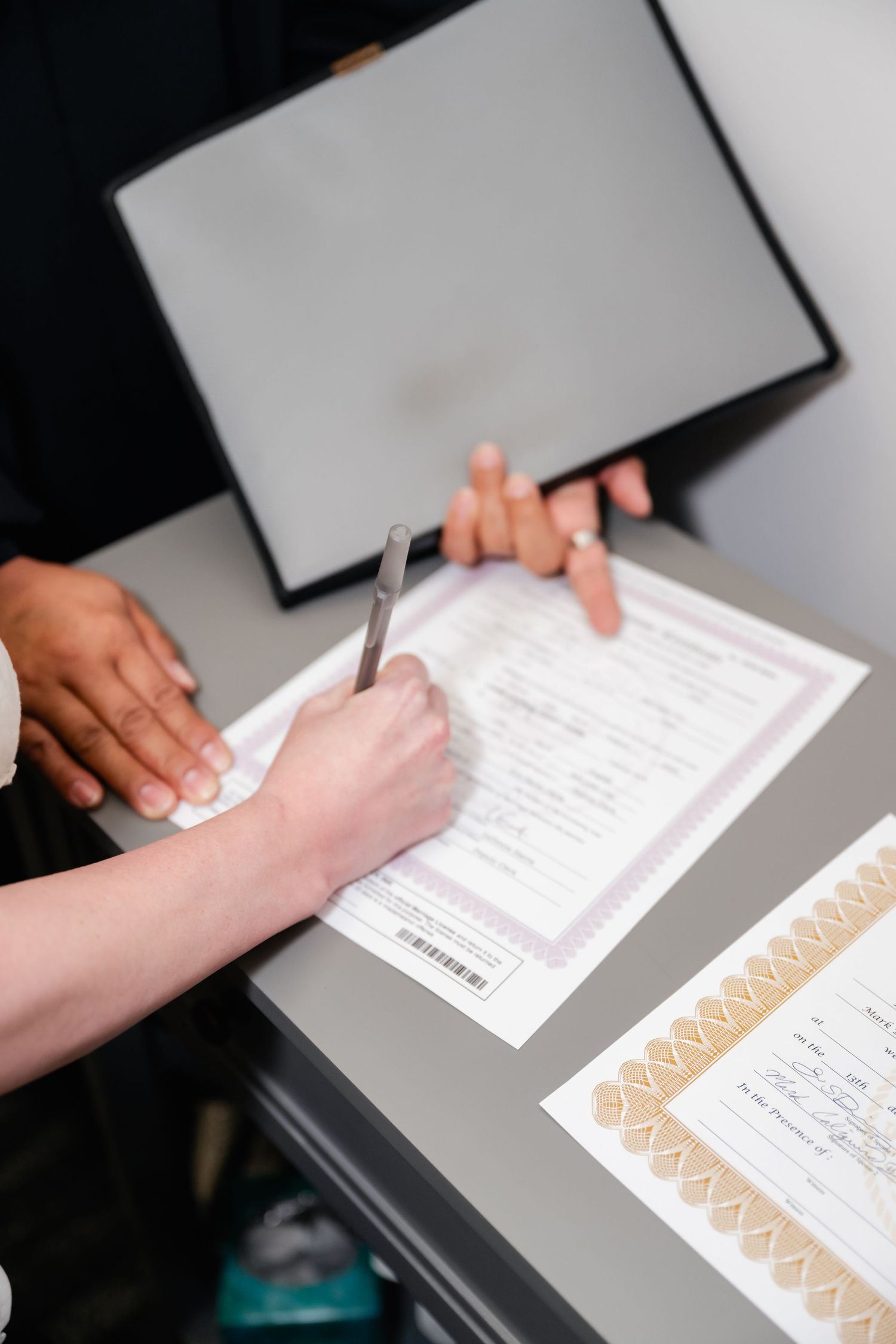 Close-up view of hands signing official documents on a desk with paperwork.