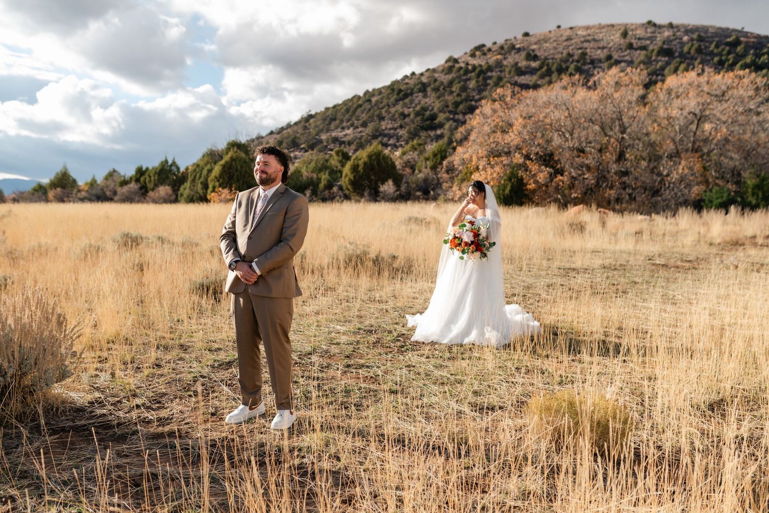 A couple poses together in a scenic mountain field with golden autumn grass and dramatic cloudy skies.