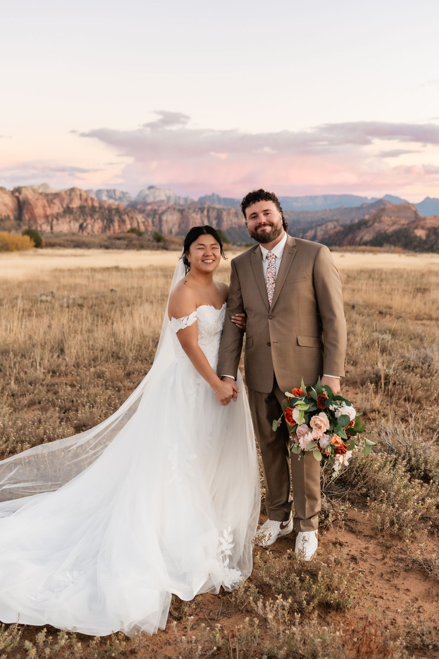 A joyful wedding portrait in a field with dramatic mountain scenery.