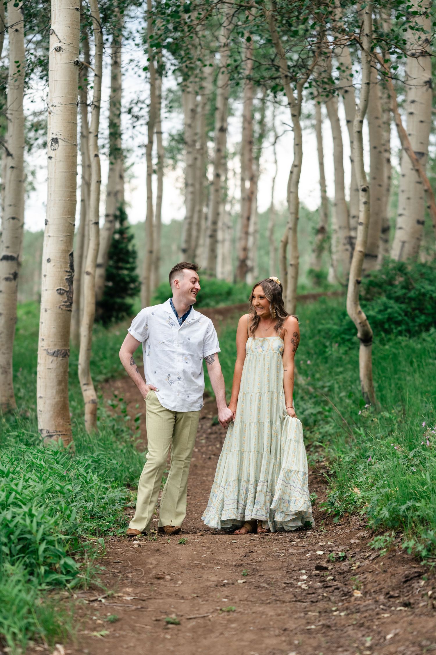 A couple strolls hand in hand down a forest trail surrounded by tall aspen trees.