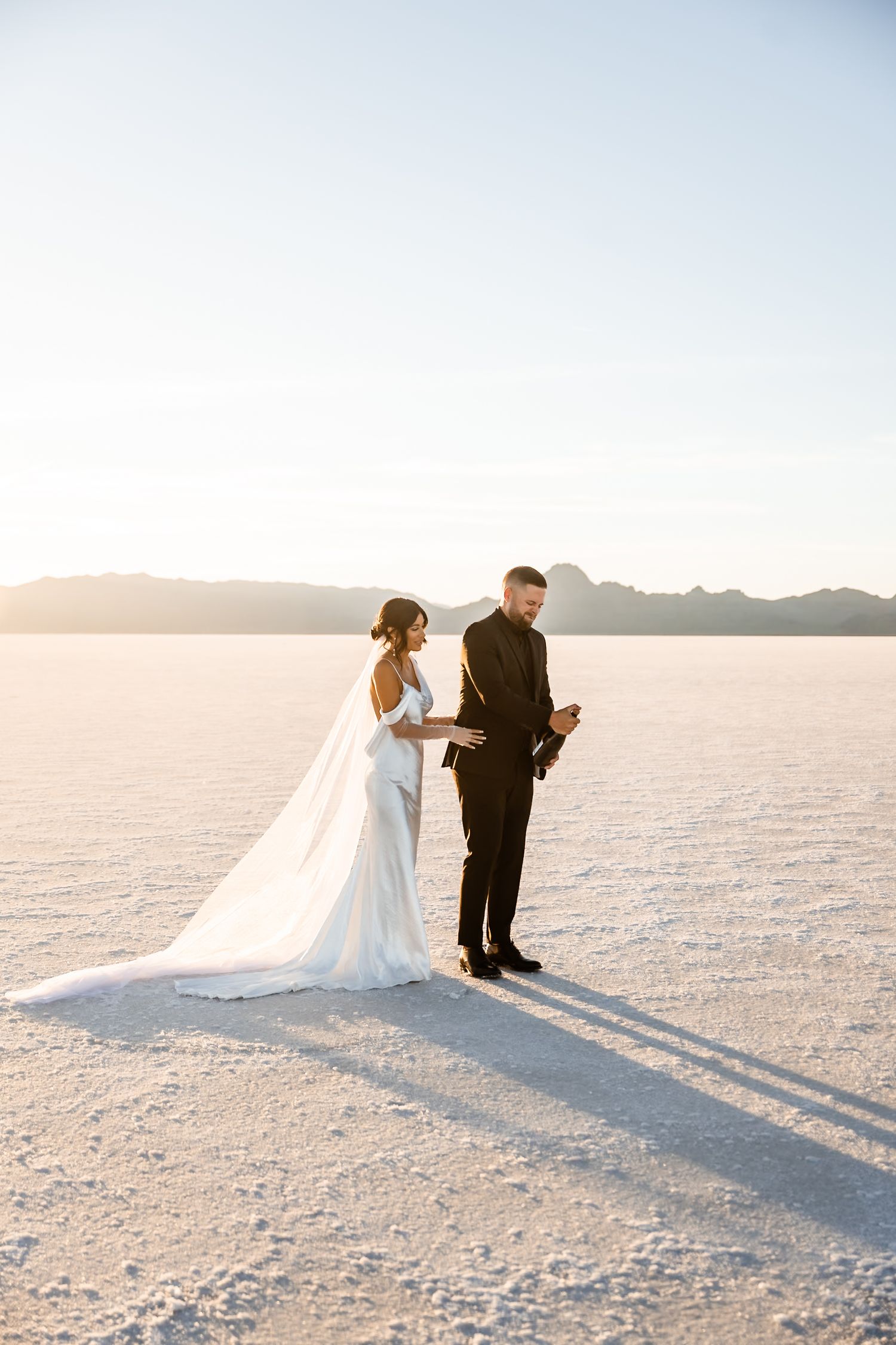 Wedding couple walks and poses on vast white salt flats during sunset photoshoot.
