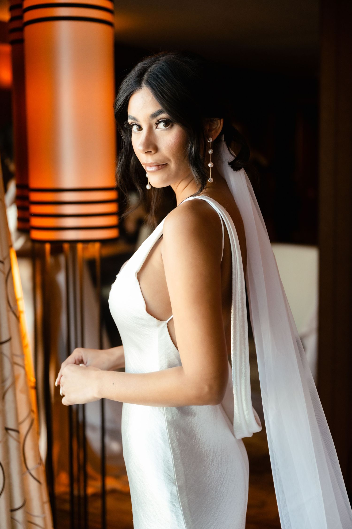 Elegant white wedding dress with flowing veil captured in warm ambient lighting.
