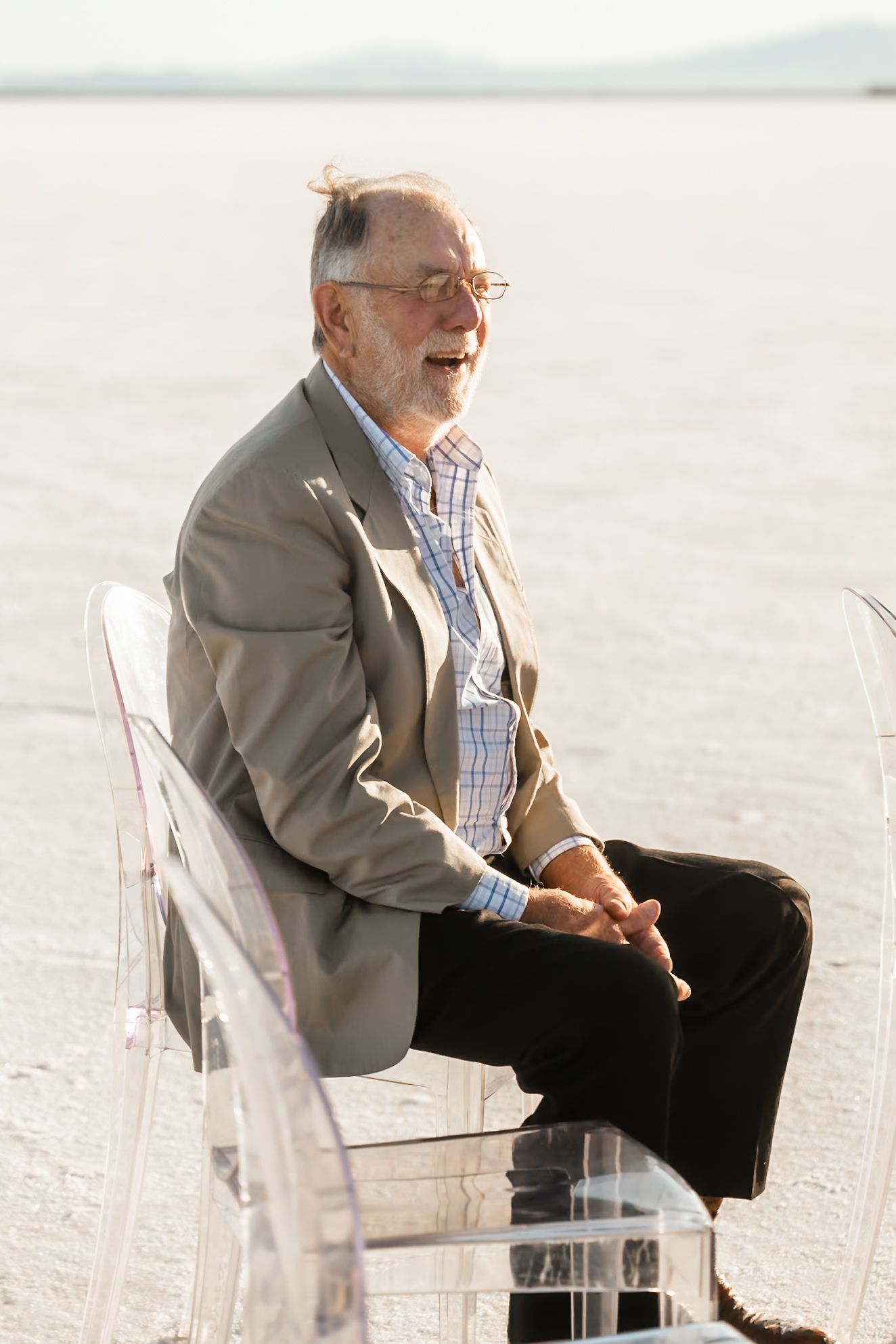 Guest seated in clear acrylic chair on salt flats during outdoor wedding ceremony.