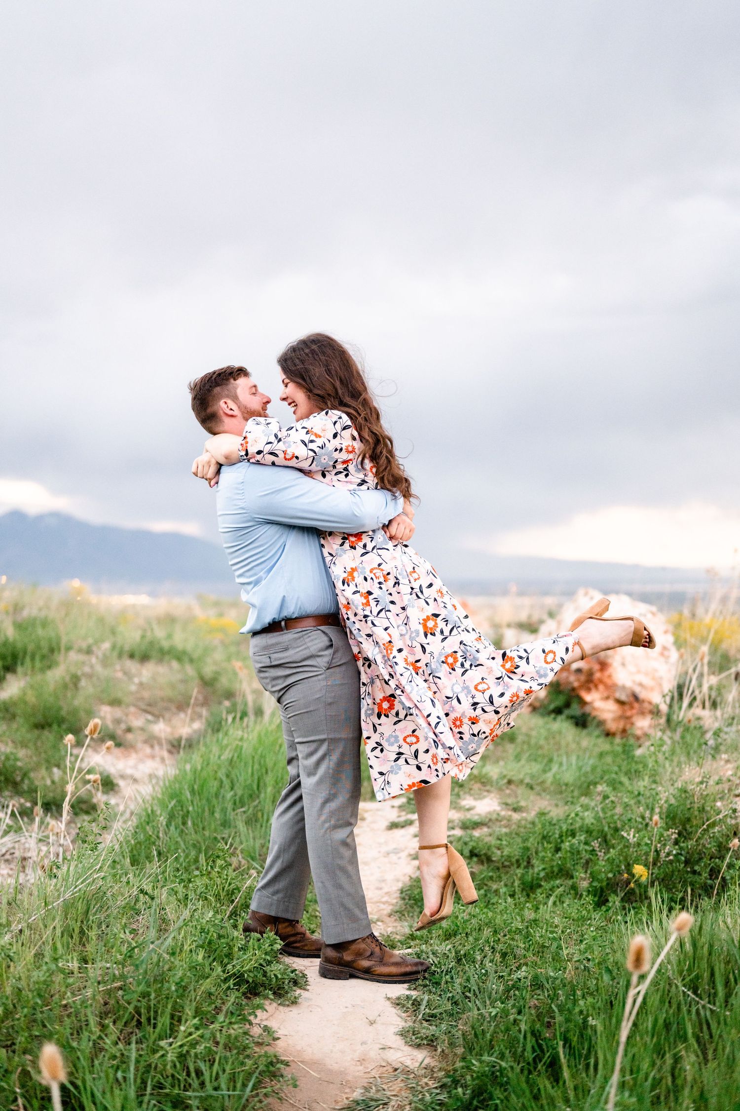 A couple embraces joyfully in a field with mountains visible in the background.