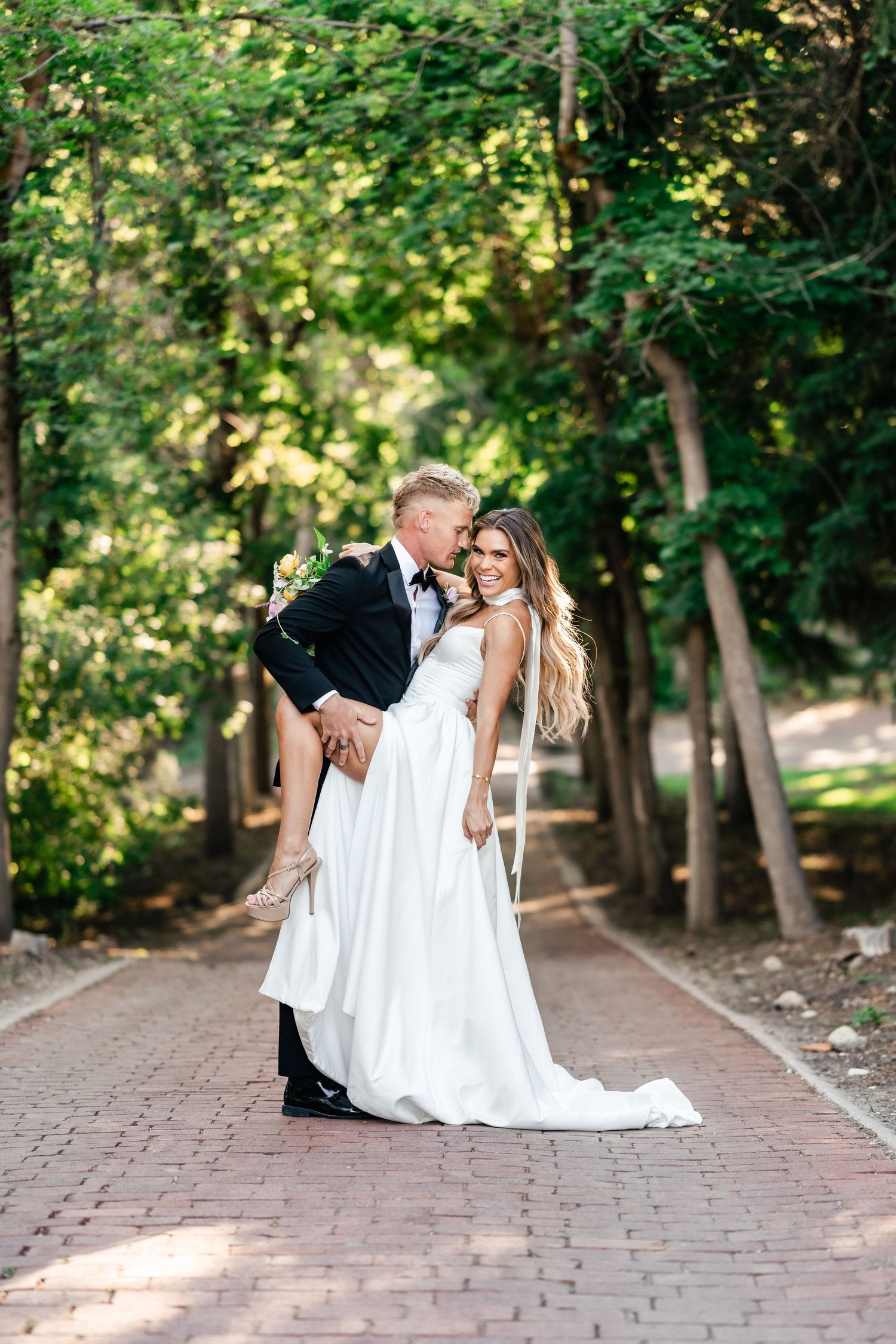 Romantic wedding portrait on brick pathway with lush green garden backdrop.