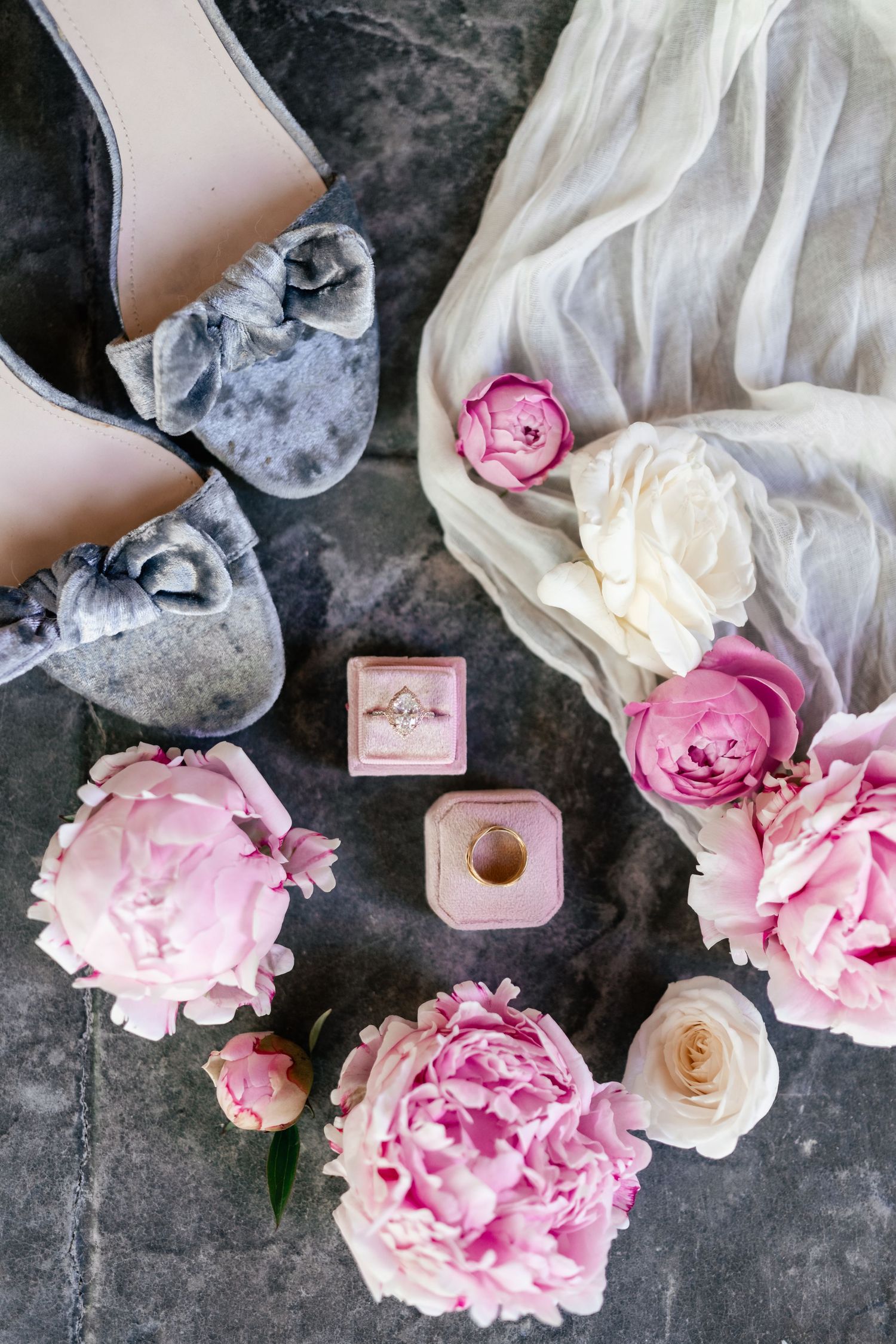Pink and white roses arranged with a small engagement ring box on a dark textured surface in a wedding proposal setup.