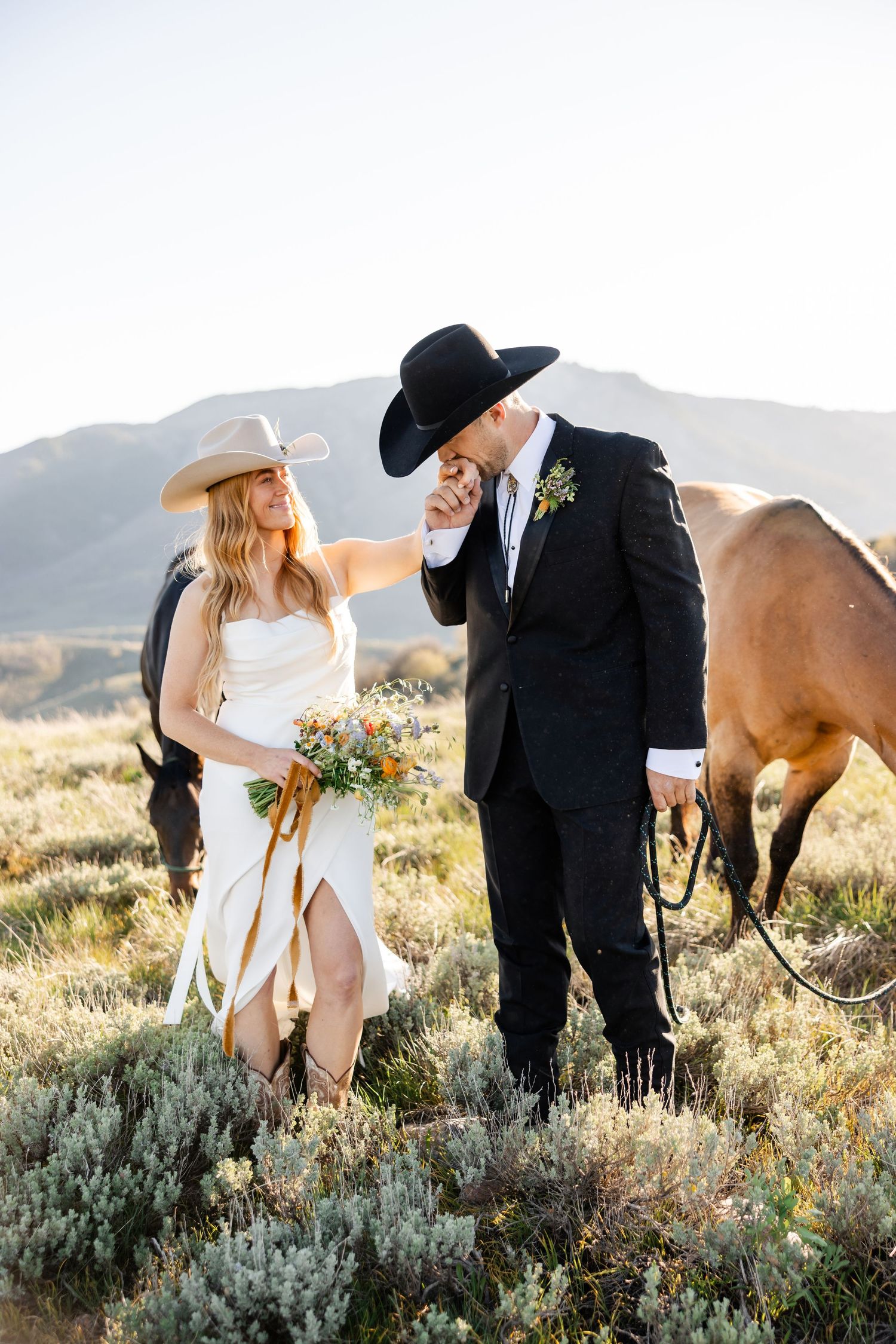Romantic wedding couple poses with horse in golden mountain meadow in the mountains of Northern Utah during their mountain elopement.