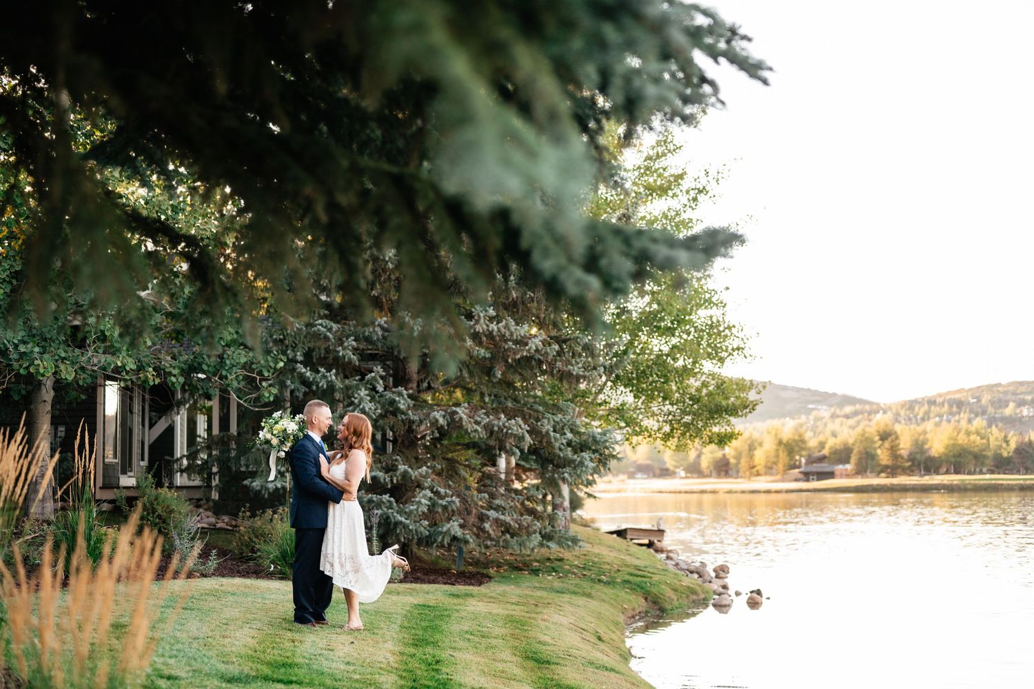 A couple shares an intimate moment during their wedding photoshoot in a scenic outdoor setting with tall trees.