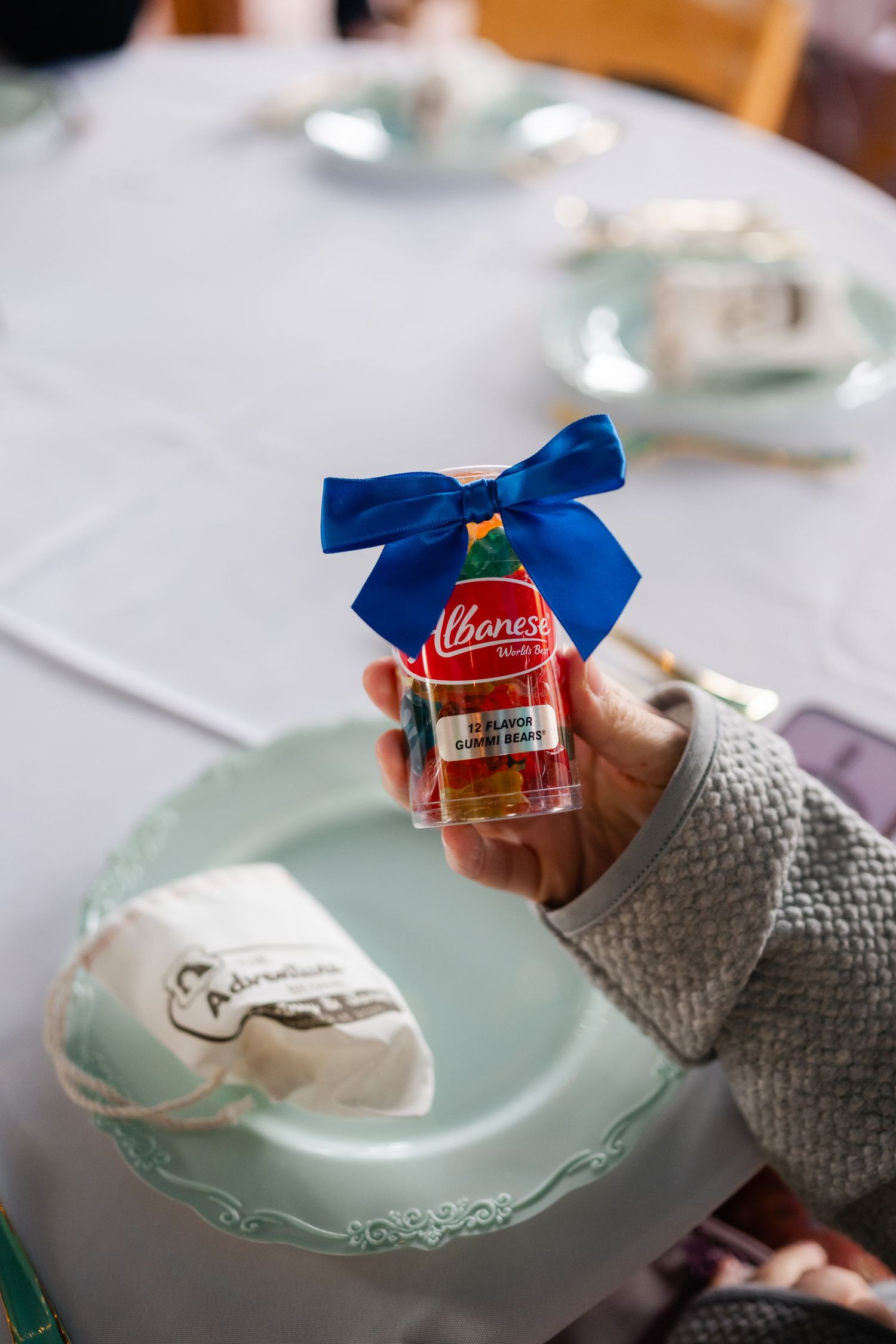 Hands holding small favor jars decorated with blue bows against a light blue plate setting.