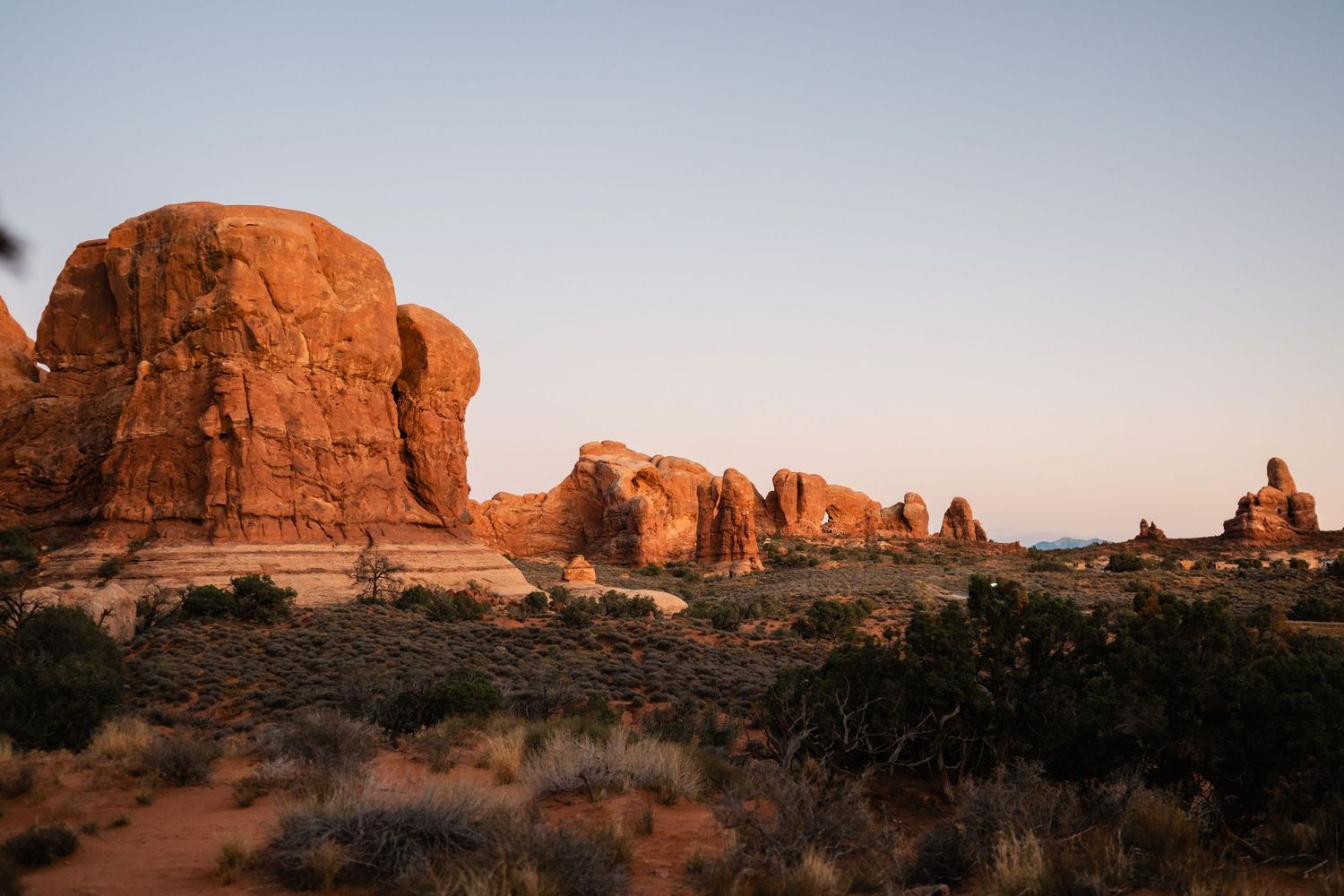 Sweeping desert landscape with towering red rock formations at dusk.