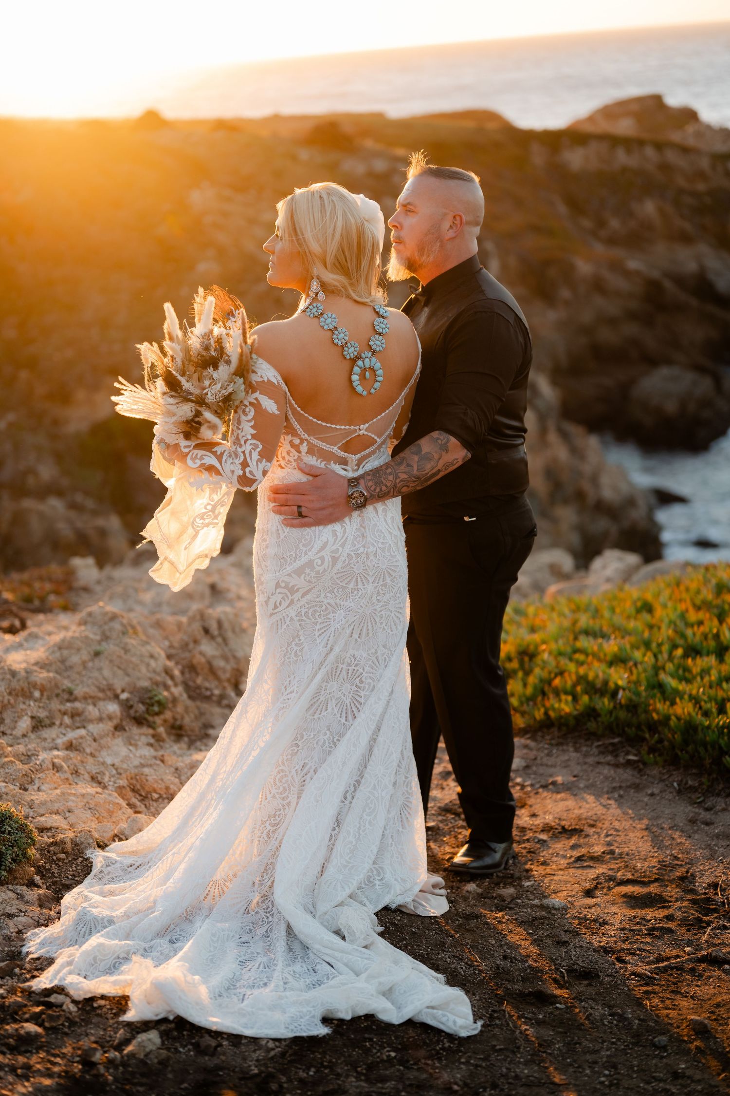 A sunset wedding portrait on a rocky coastal cliff with dramatic ocean views.