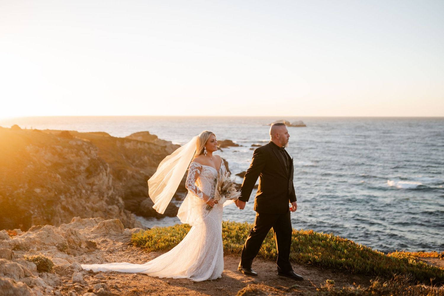 Wedding ceremony silhouetted against dramatic coastal sunset.