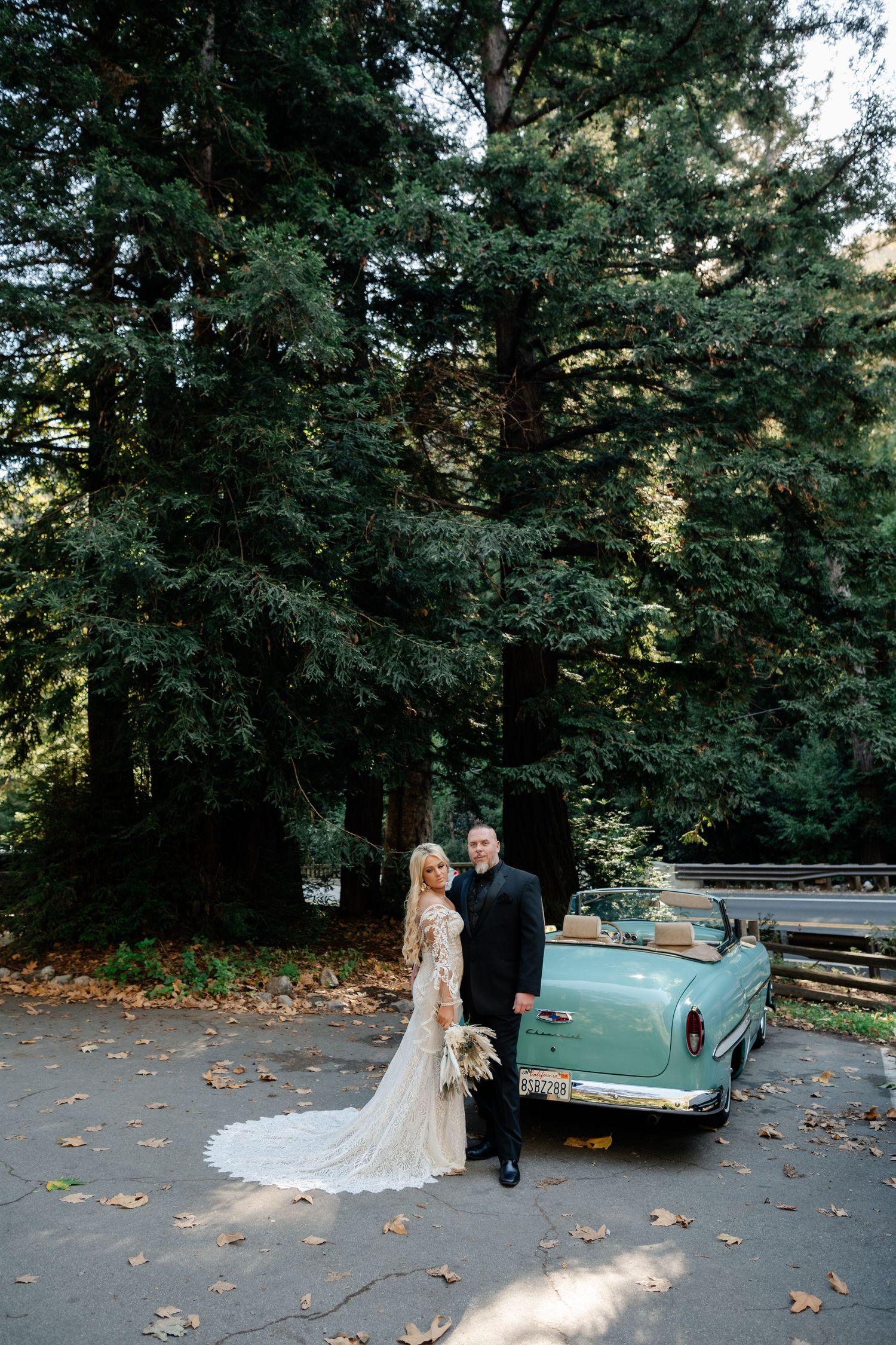 Classic mint green vintage car parked among tall trees in forest setting.
