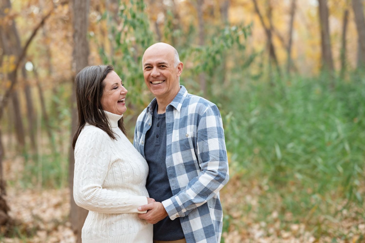 A couple shares a joyful moment together in a wooded outdoor setting during autumn.