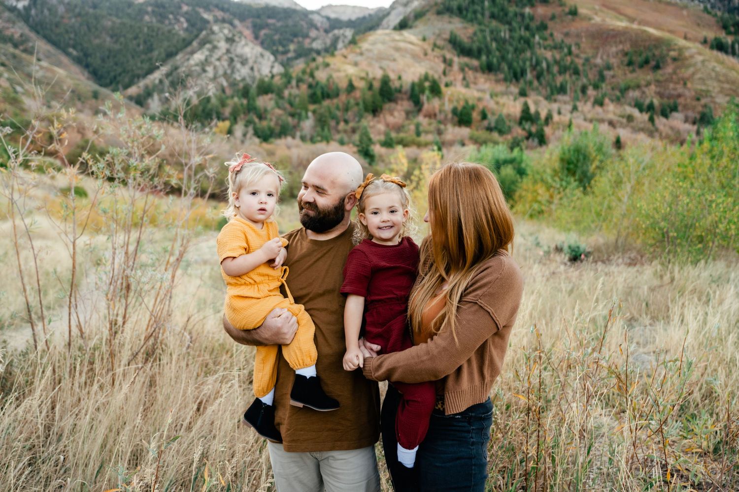 A family enjoys candid moments together in a mountain field with golden grass.