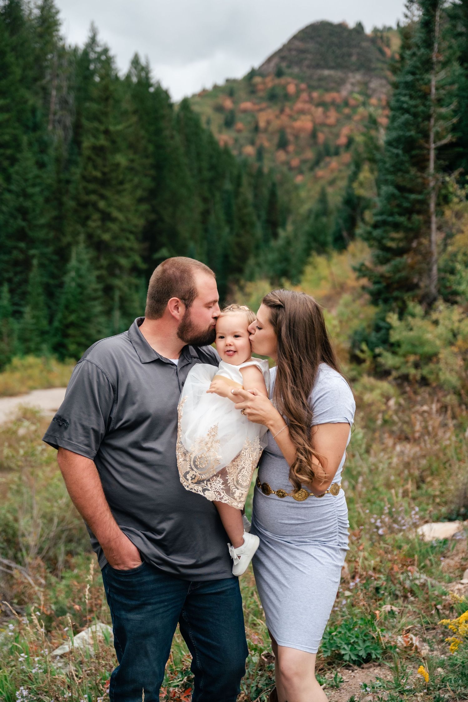 A family shares tender moments together in a scenic mountain forest setting with evergreen trees and autumn colors.