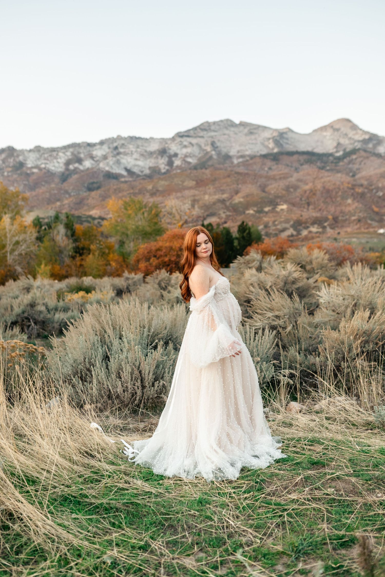 A person in a flowing white dress twirls gracefully in a desert landscape with mountains and sagebrush in the background.