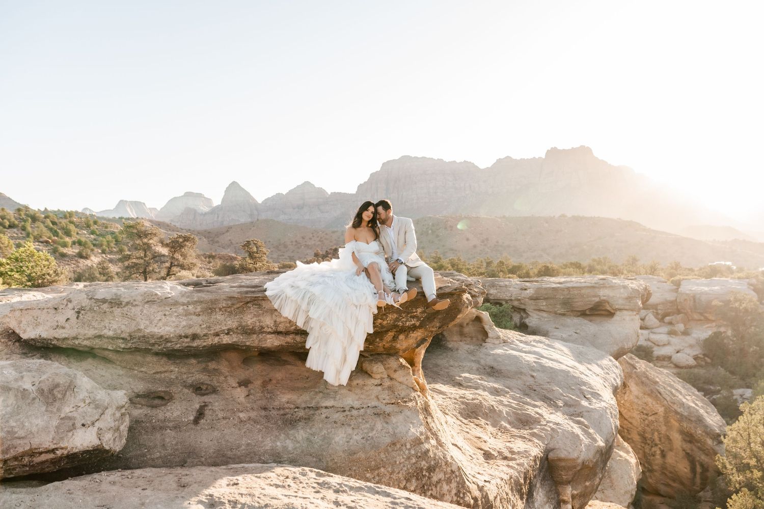 Zion Adventure Session. Couple in wedding attire embracing on scenic mountain overlook at golden hour.
