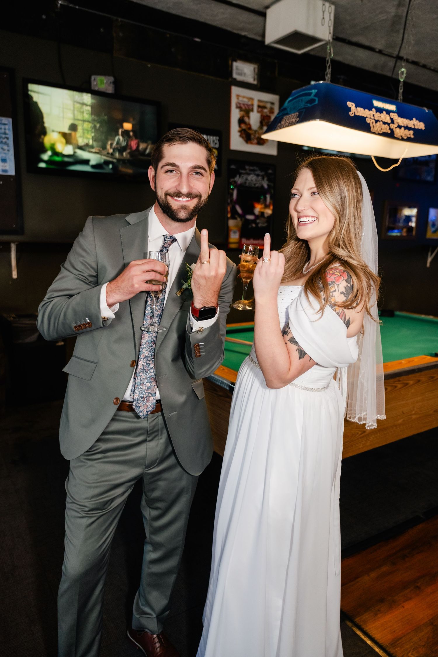 A couple in wedding attire sharing a playful moment by a pool table in a bar.