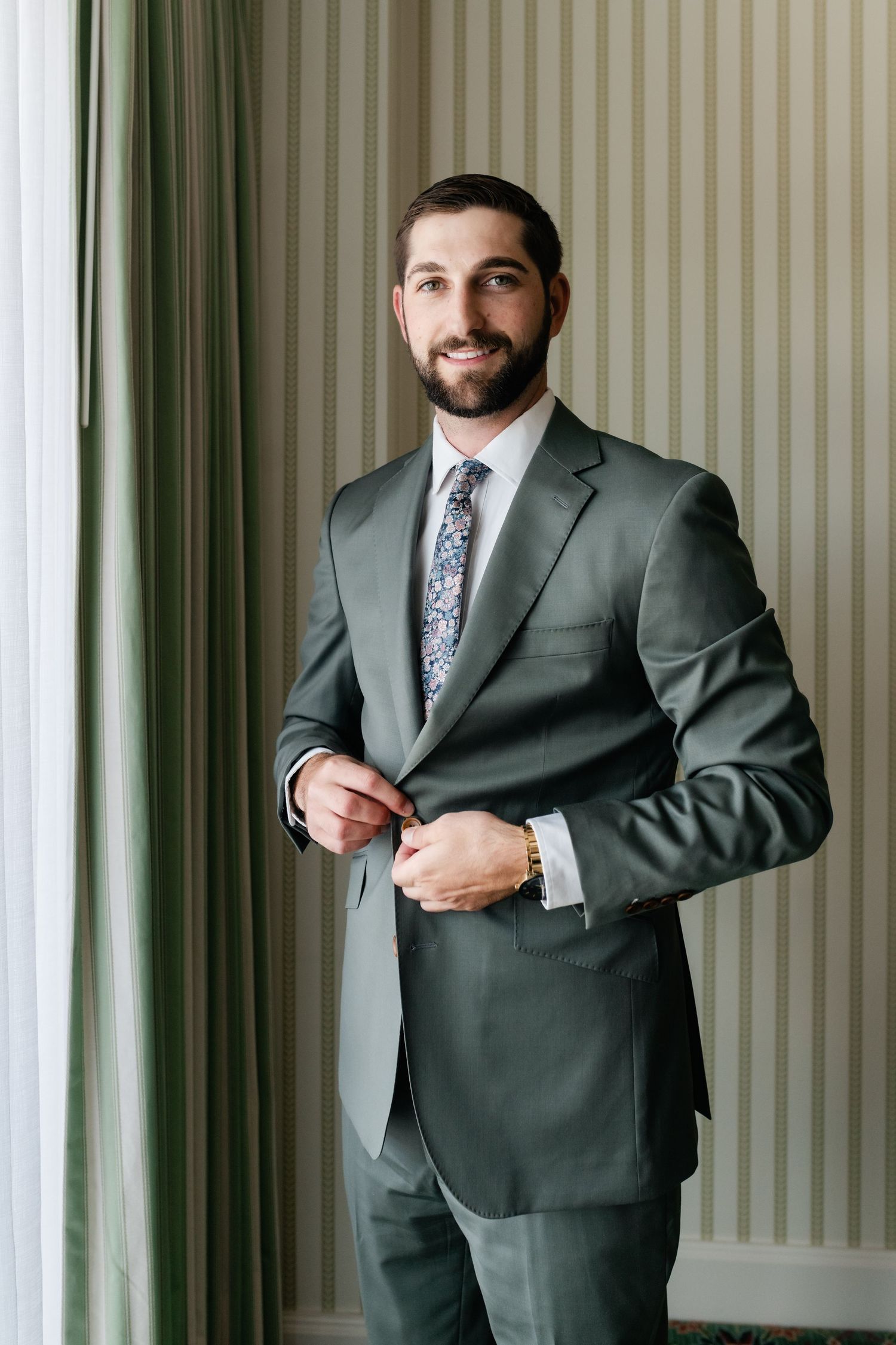 Multiple angles of someone wearing a charcoal suit and floral tie while getting dressed in a room with striped walls.