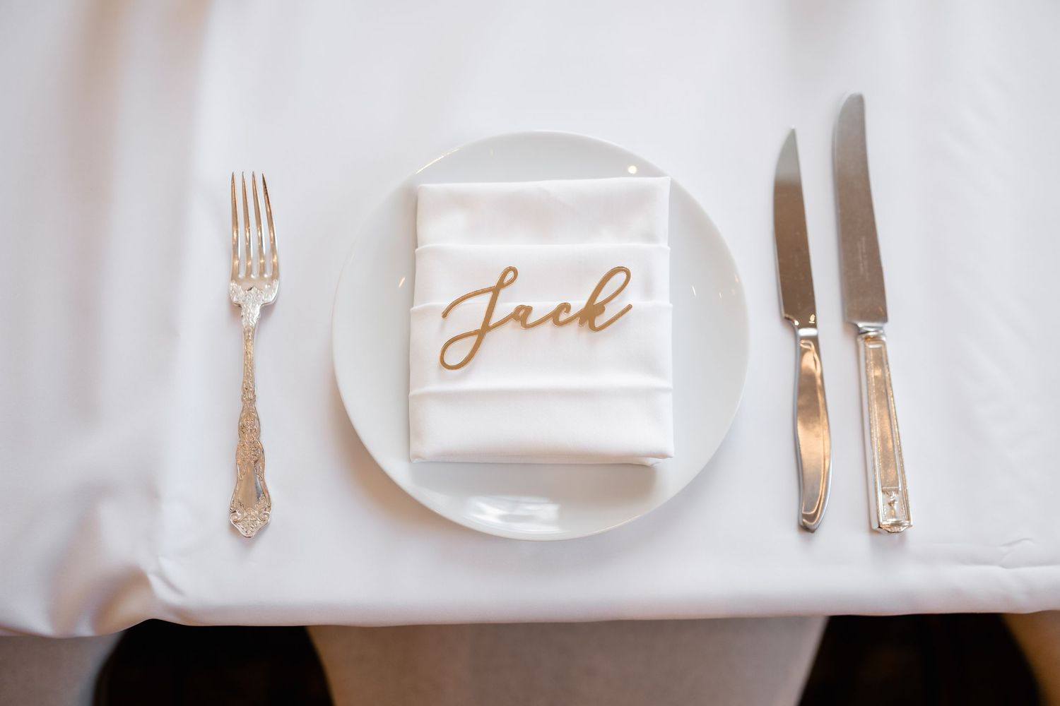 Elegant white table setting with gold calligraphy place cards and polished silverware.