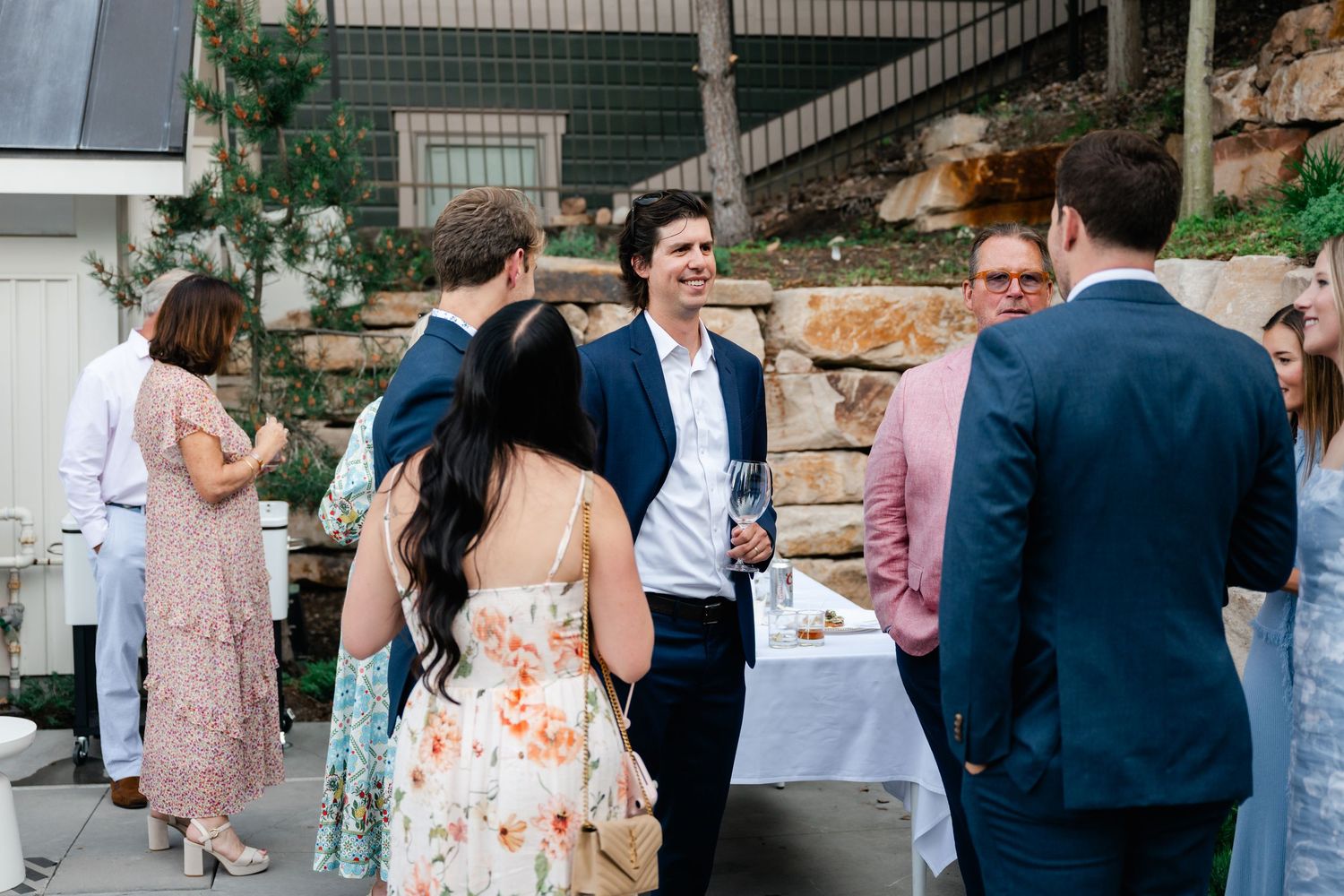 Wedding guests mingling at an outdoor reception with stone walls and casual attire.