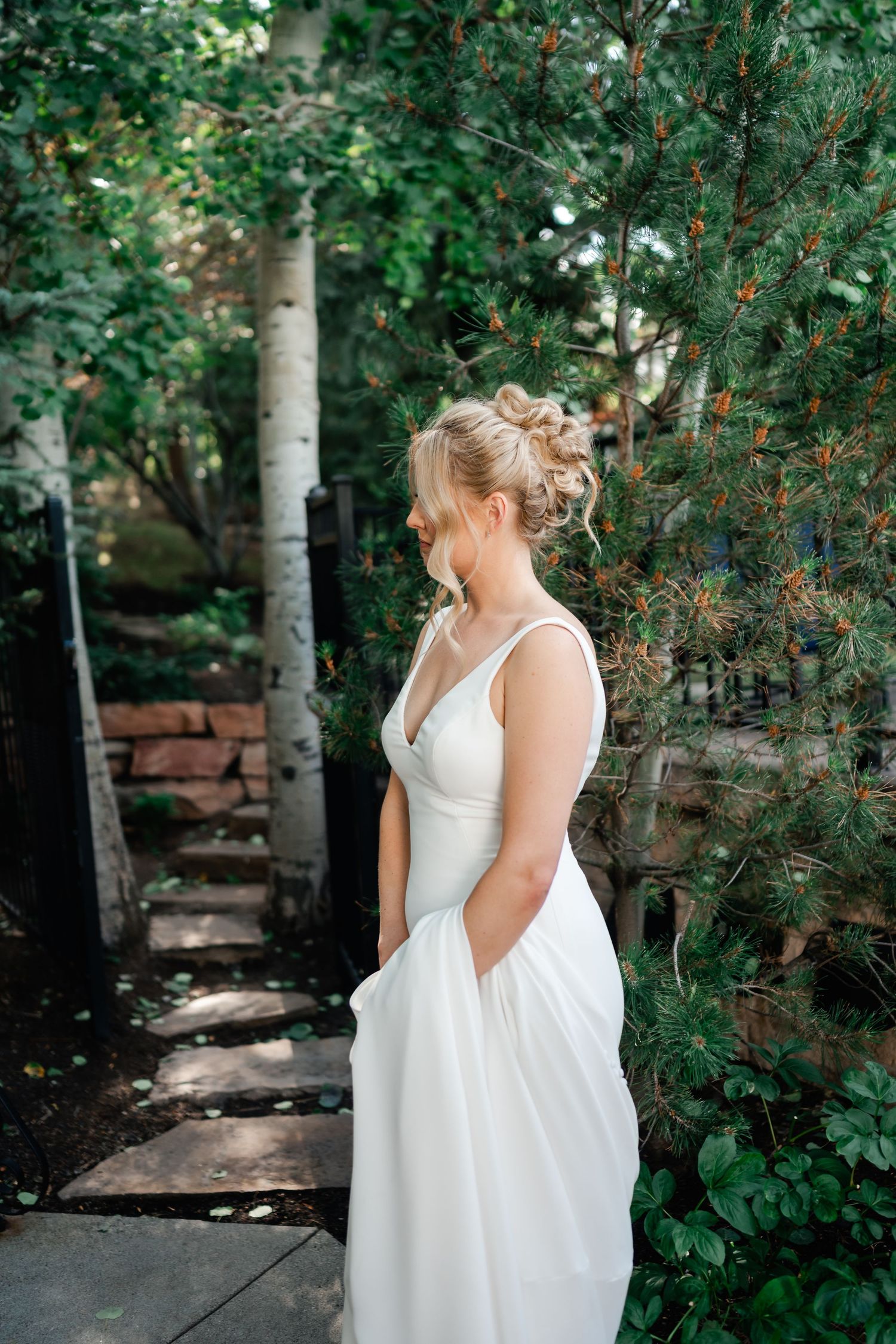 Bride in flowing white dress walks through a garden path with natural greenery.