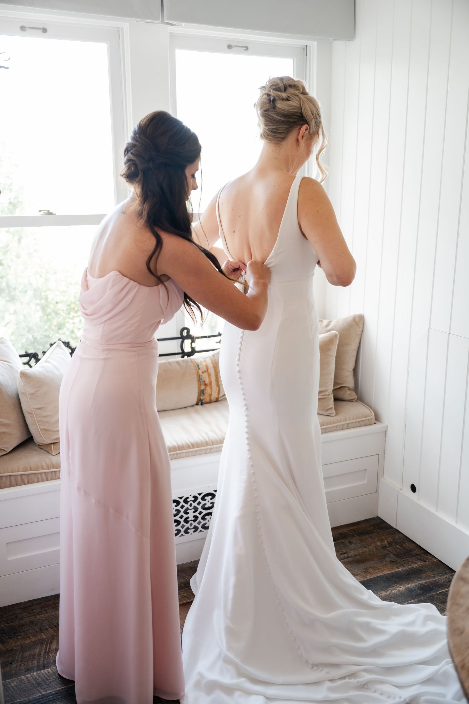Wedding preparation scene showing bridesmaids in pink dresses helping with a white wedding gown.