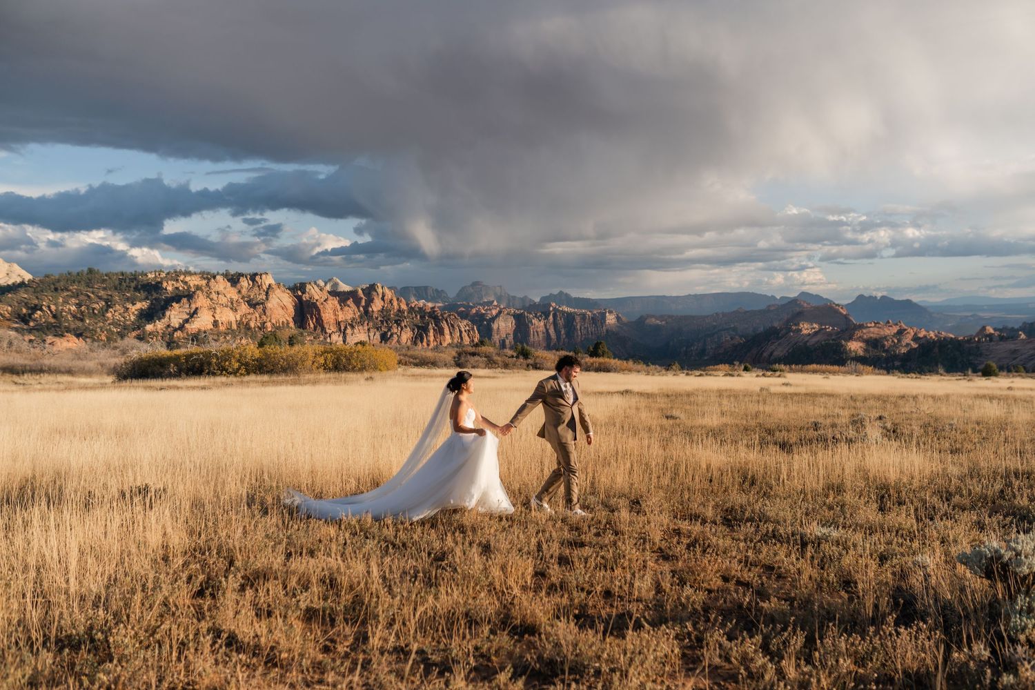 A panoramic view of a wedding celebration in a vast mountain meadow at sunset.