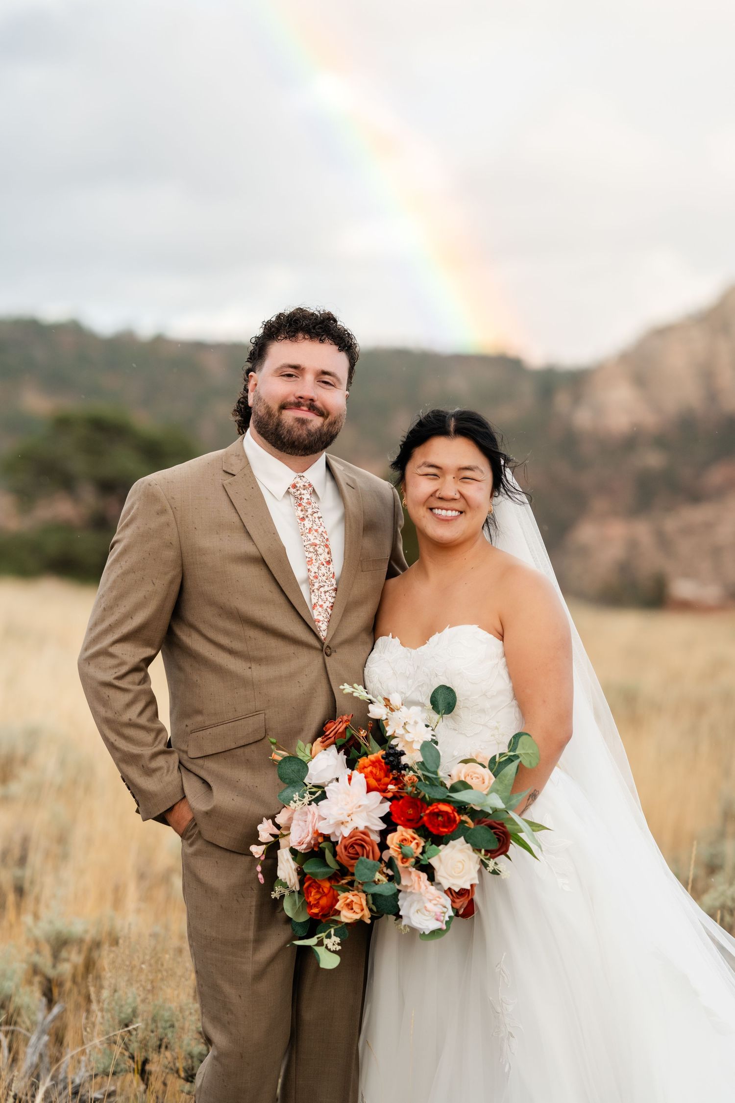 Beautiful rainbow appears during outdoor wedding photos in mountain field with autumn colors.