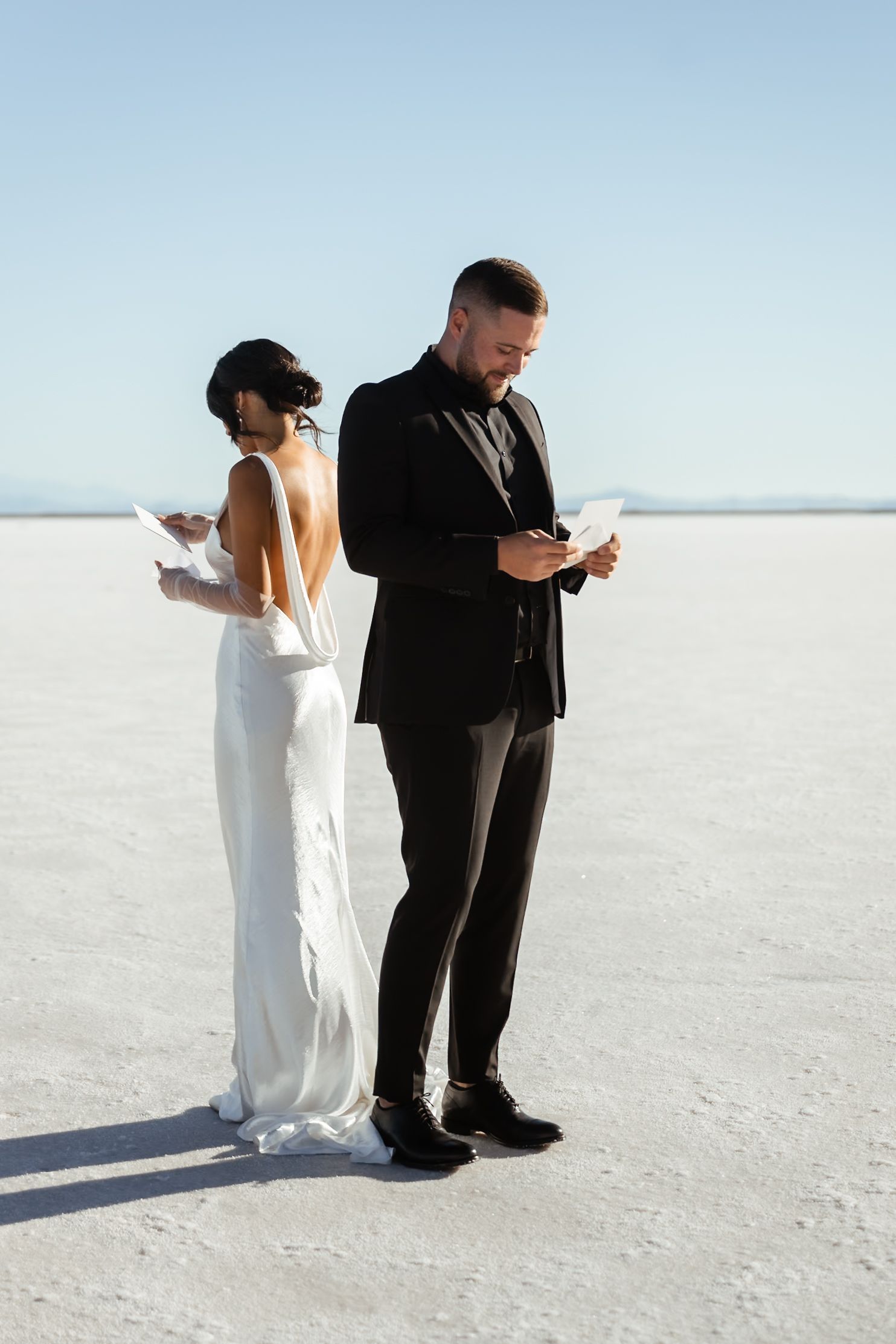 Couple reading vows while standing on bright white salt flats under blue sky.