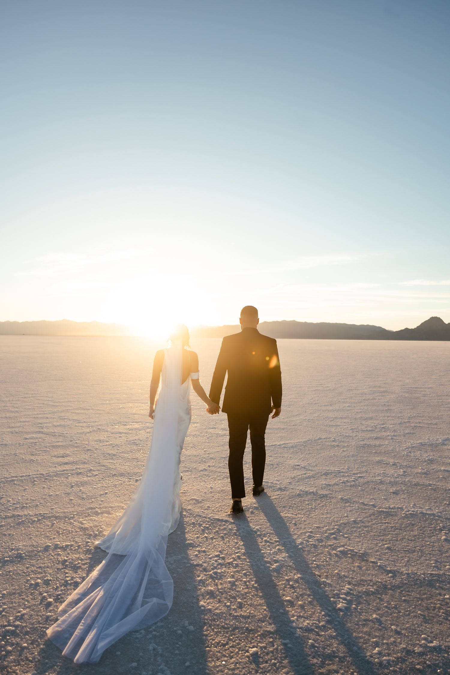 Long shadows stretch across salt flats as a couple walks during golden hour.