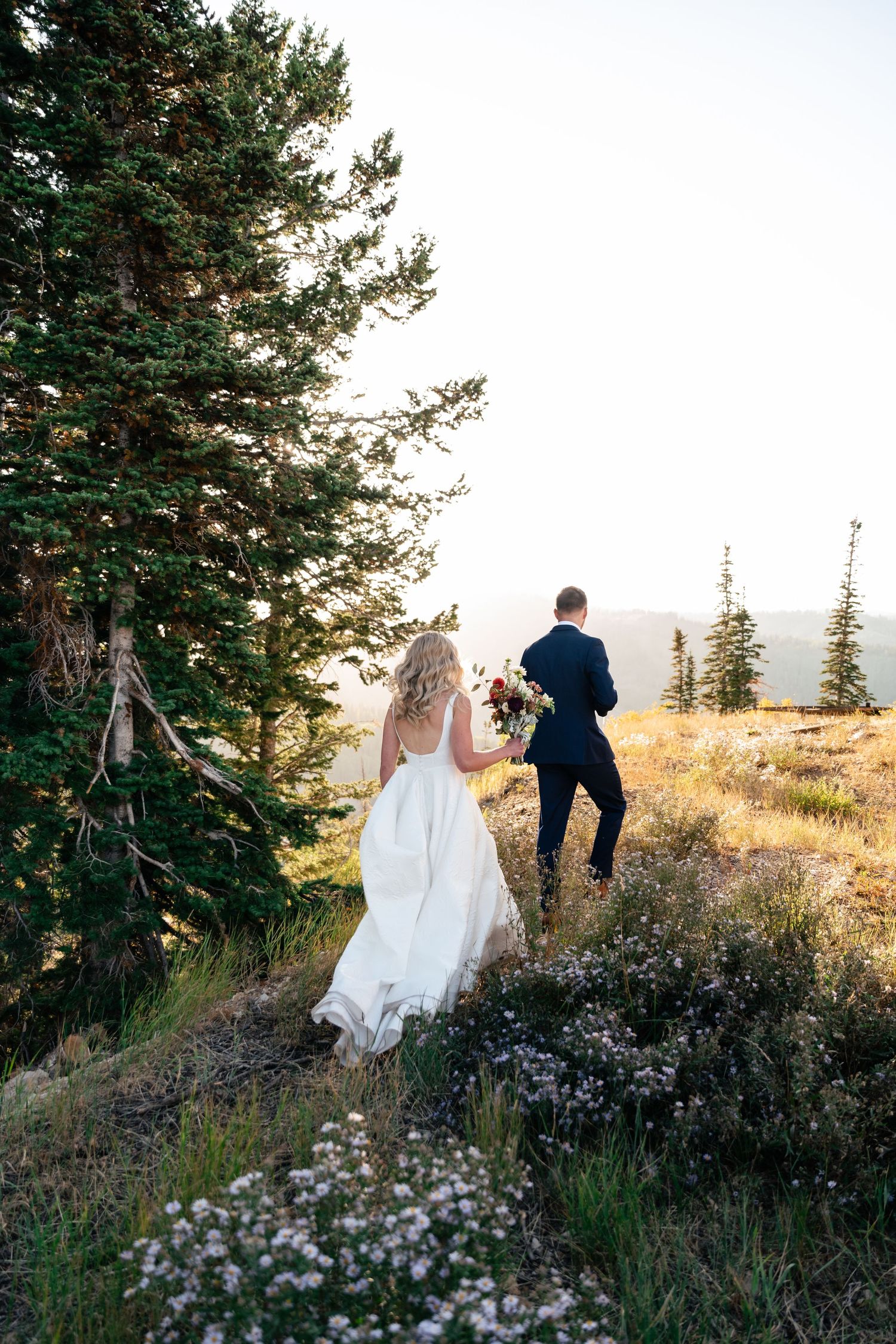 Couple walking through wildflowers on a mountain hillside at sunset.