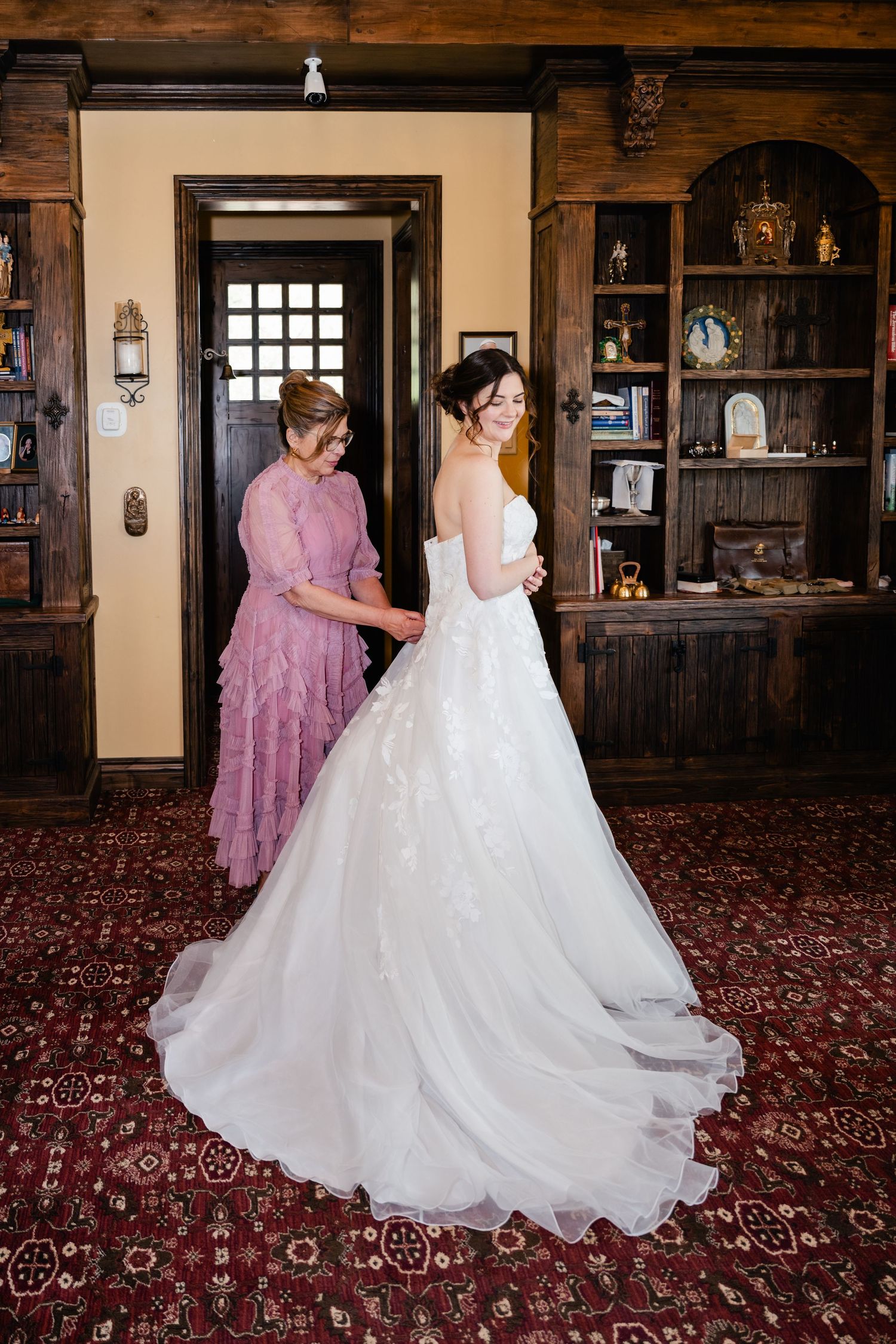 Wedding dress preparations in an elegant room with ornate carpeting and wooden decor.