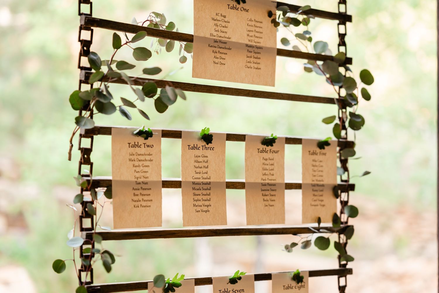 A rustic wooden seating chart display decorated with greenery at a wedding venue.