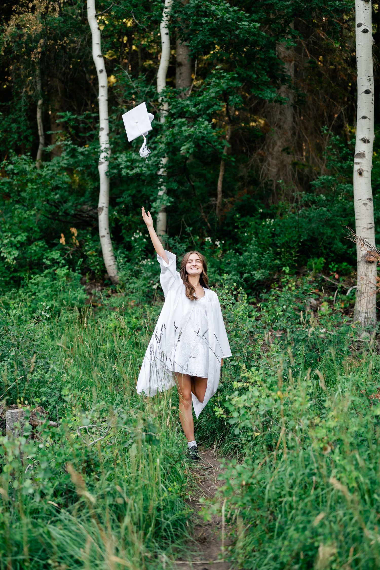 Two people walking through a lush forest path surrounded by aspen trees and green summer foliage.