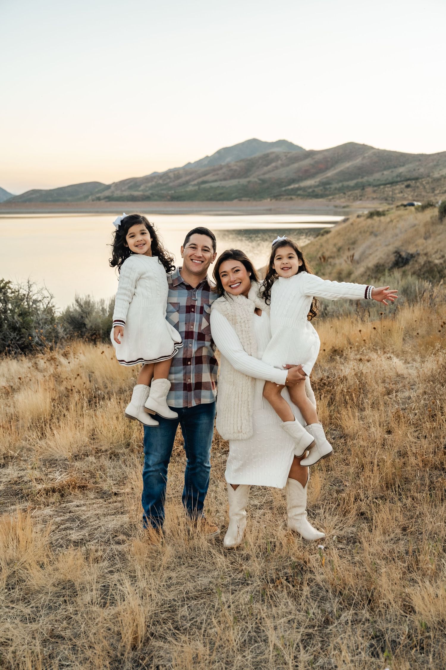 A family poses together in casual attire against a scenic mountain backdrop during golden hour.