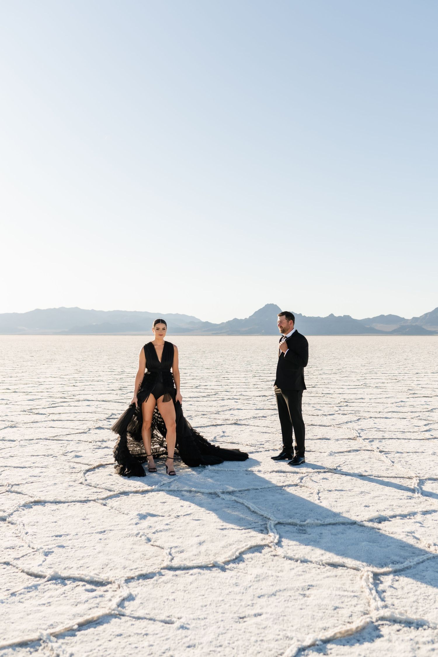 Salt Flats Photographer. Formal couple poses dramatically on white salt flats with mountains in the distance.