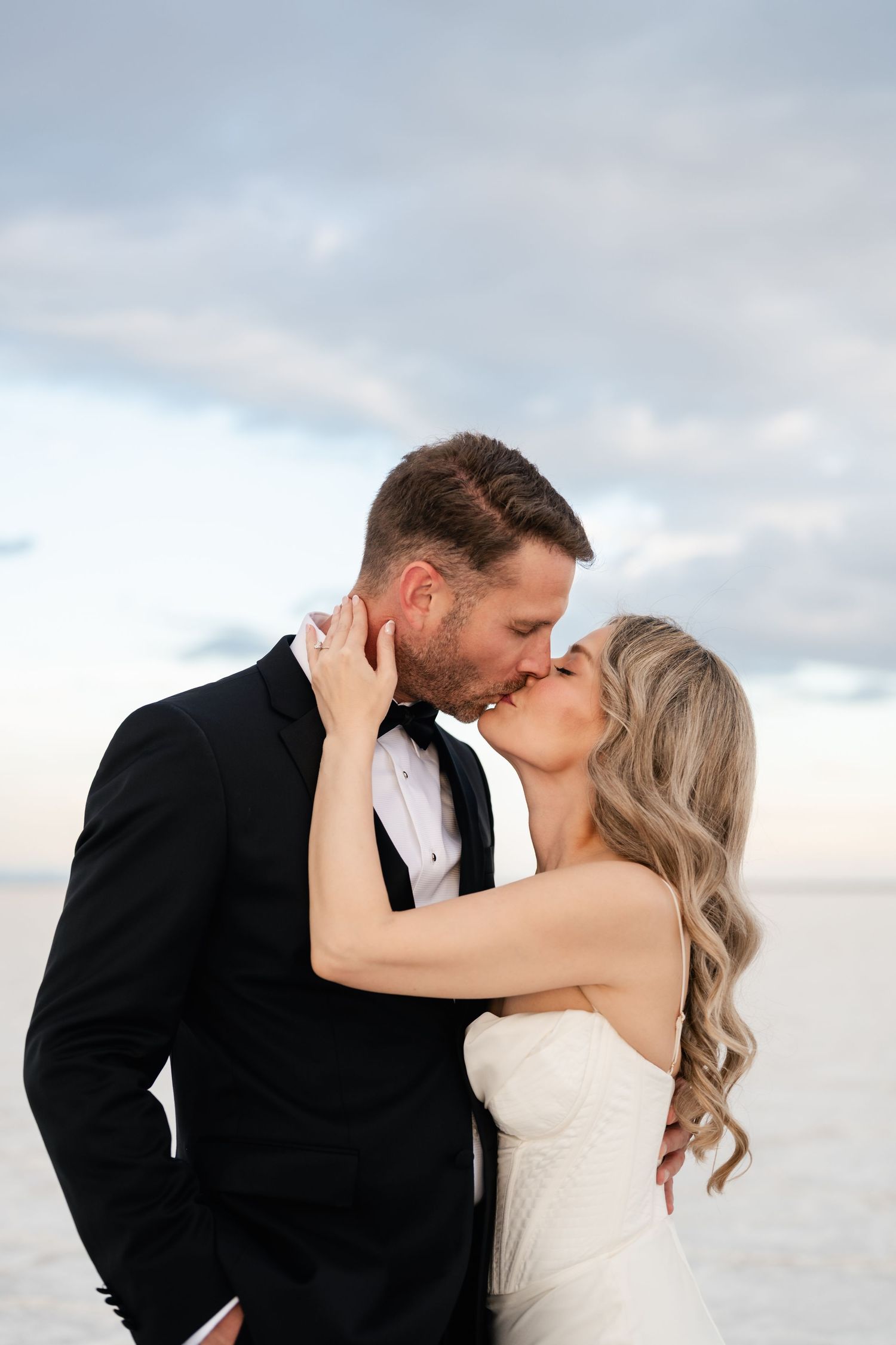 Salt Flats Elopement Photographer. A romantic wedding couple shares intimate kisses against a cloudy sky backdrop.