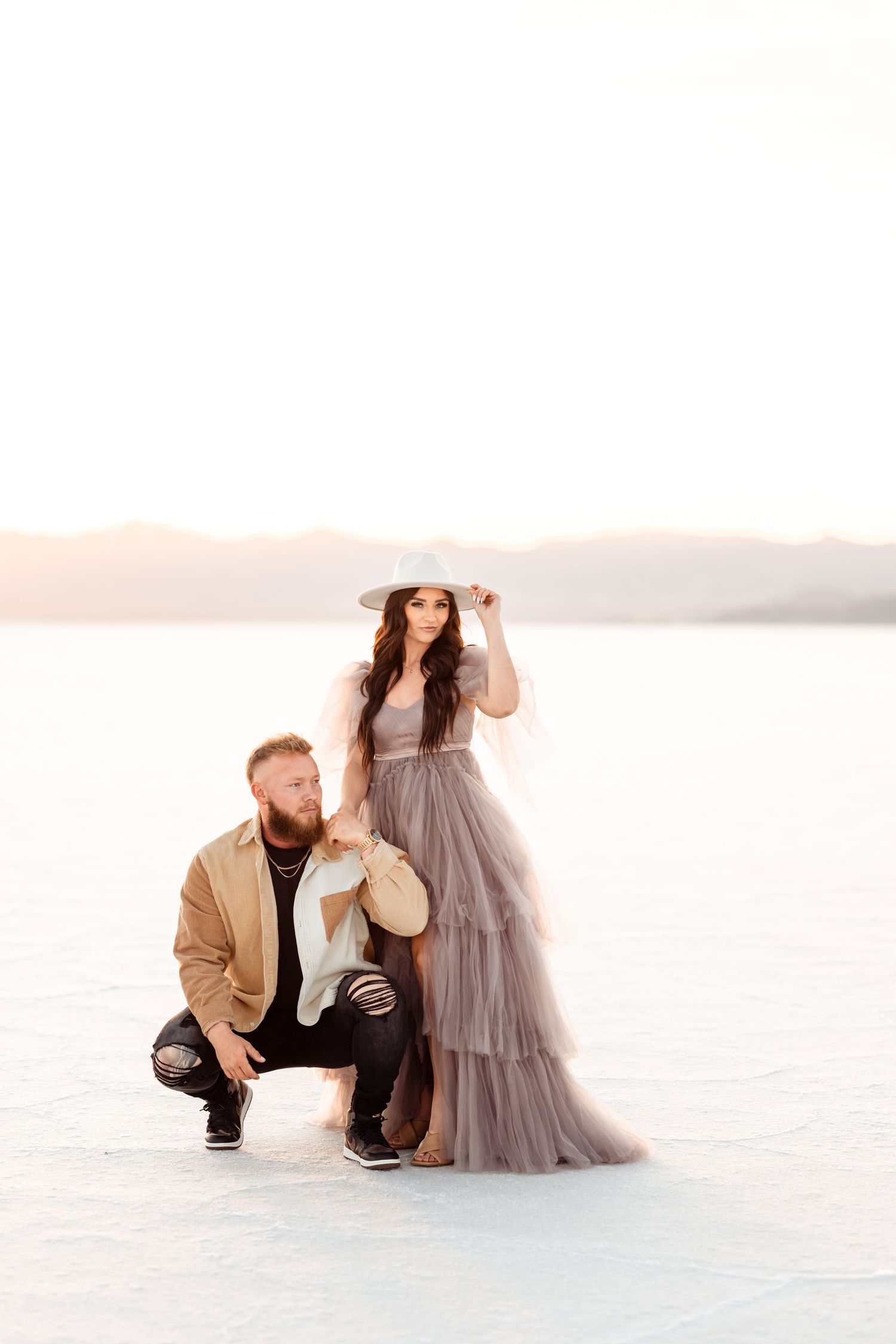 Utah Salt Flats Photographer. Couple poses intimately on salt flats with woman in flowing gray dress and wide-brim hat.