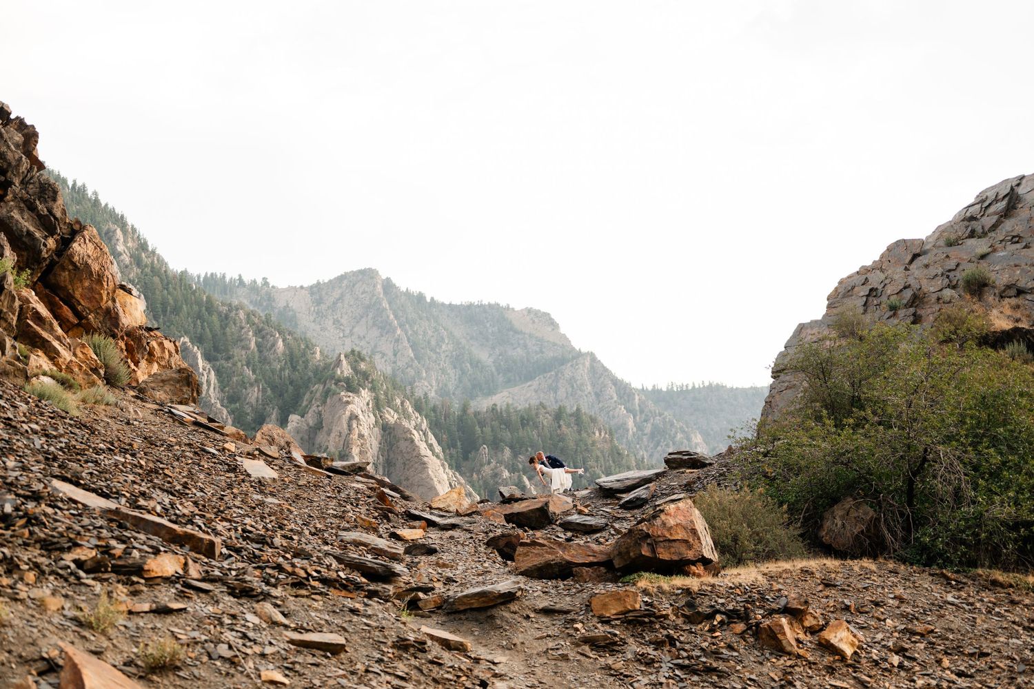 A rocky mountain landscape with stone cairns and evergreen trees under an overcast sky.