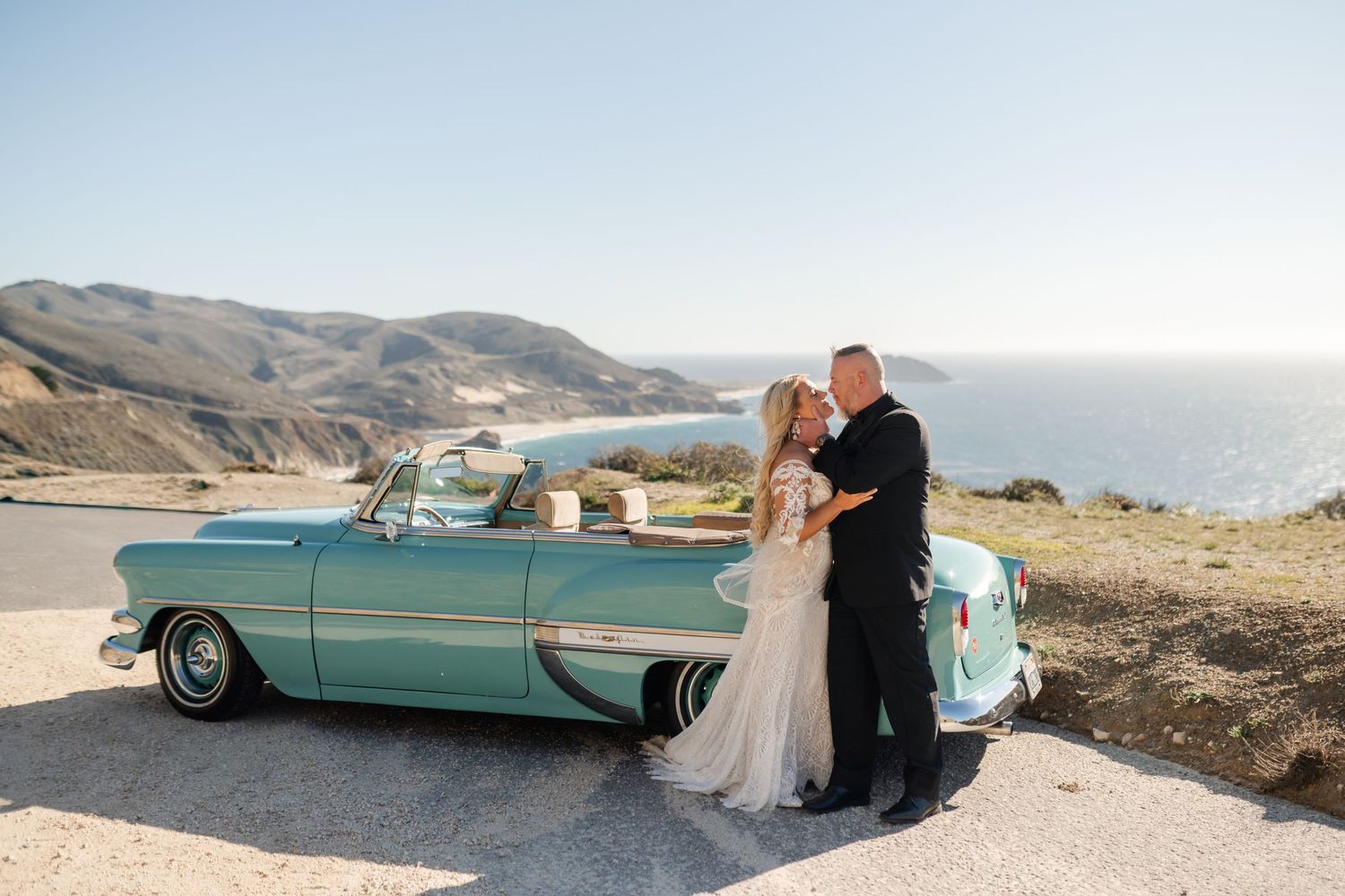 Classic turquoise convertible parked on coastal cliff overlooking the ocean during a wedding photoshoot.