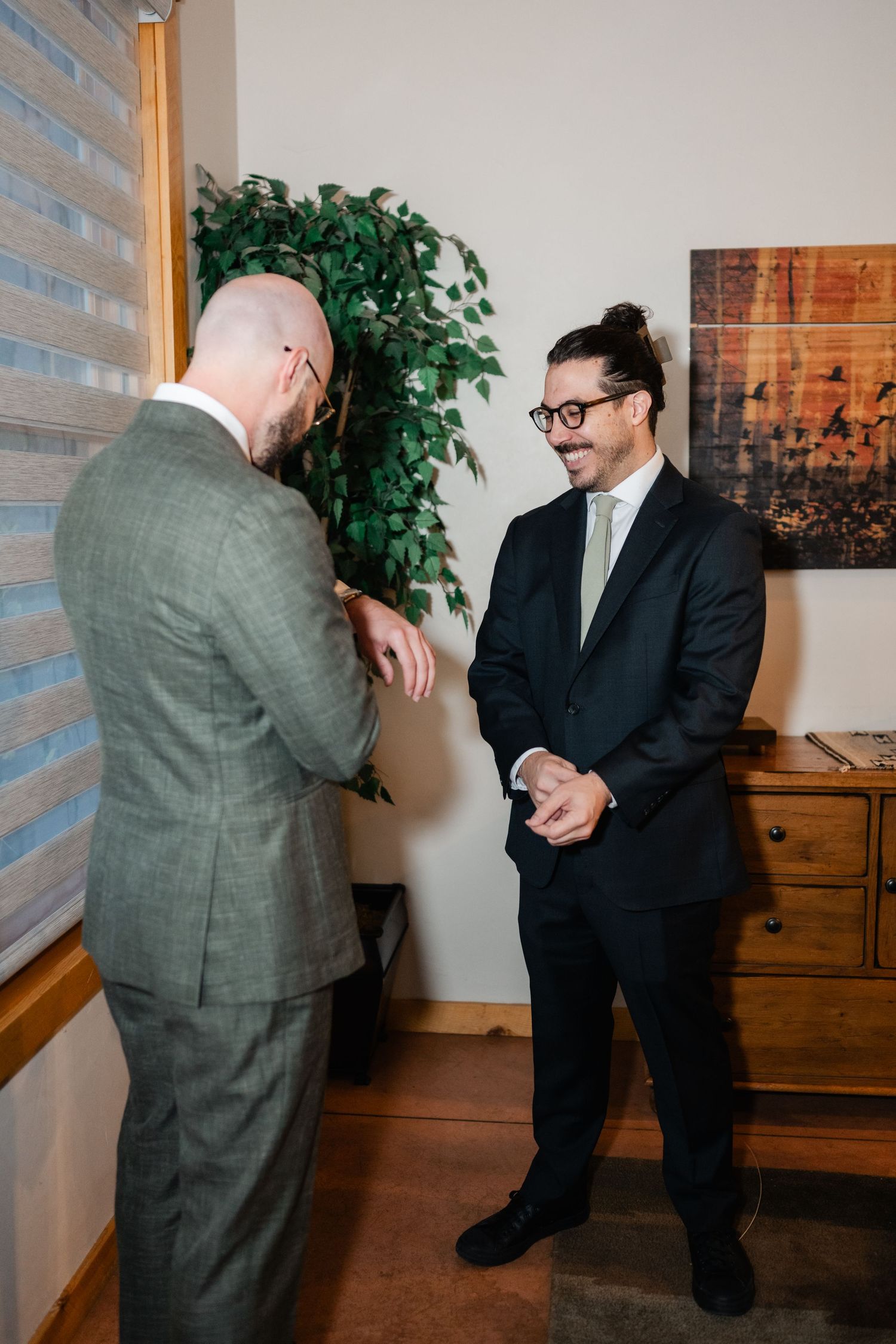 Two people in formal wear interact playfully in an indoor setting with window blinds.