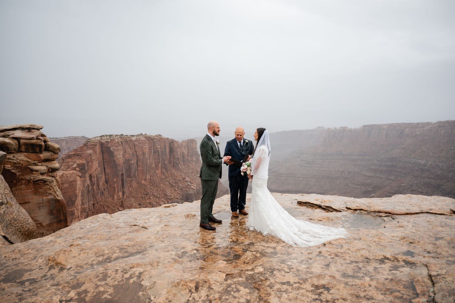 Wedding group positioned on rocky desert overlook with dramatic canyon backdrop.