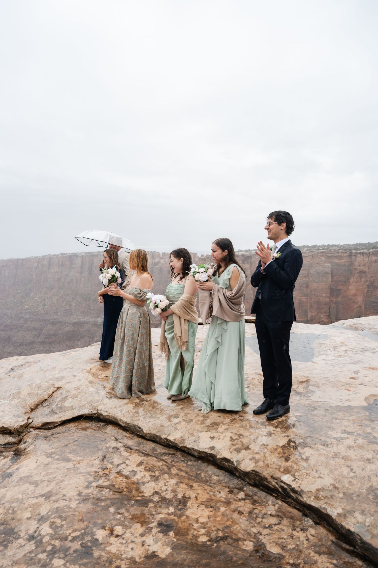 Wedding party lined up on canyon edge in formal attire during cloudy day.
