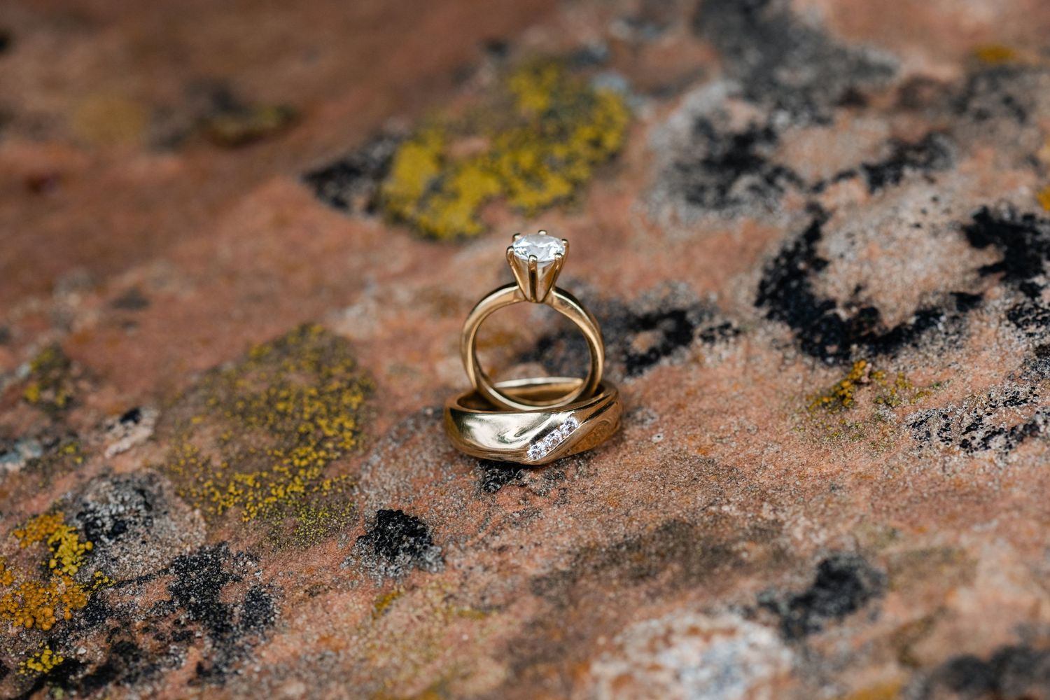 Wedding rings photographed on textured pink stone with natural lichen and moss details.