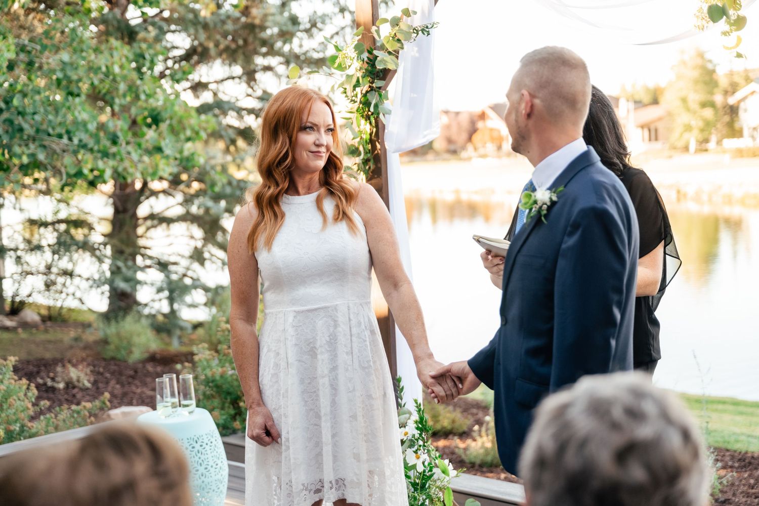 A couple shares a joyful moment during their outdoor wedding ceremony beside a lake.