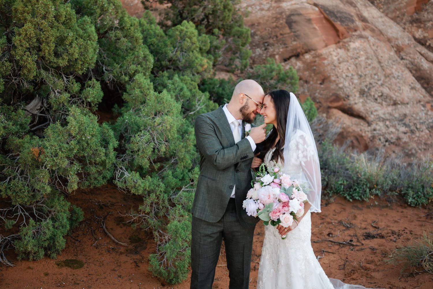 A romantic first look moment between newlyweds among red rock cliffs and desert vegetation.